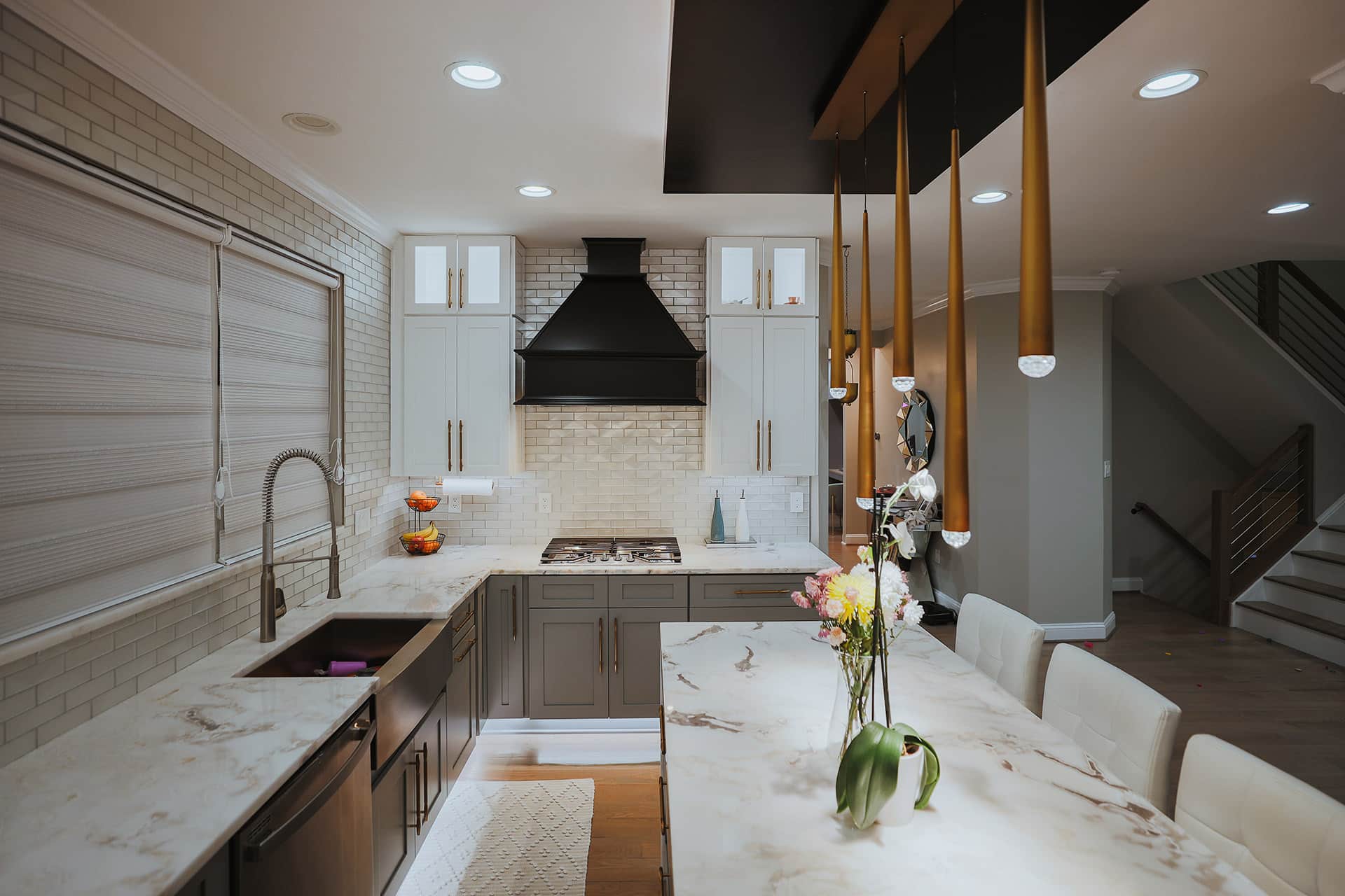 two tone kitchen with grey lower cabinets, white upper cabinets, marble countertops, and brass pendant lights