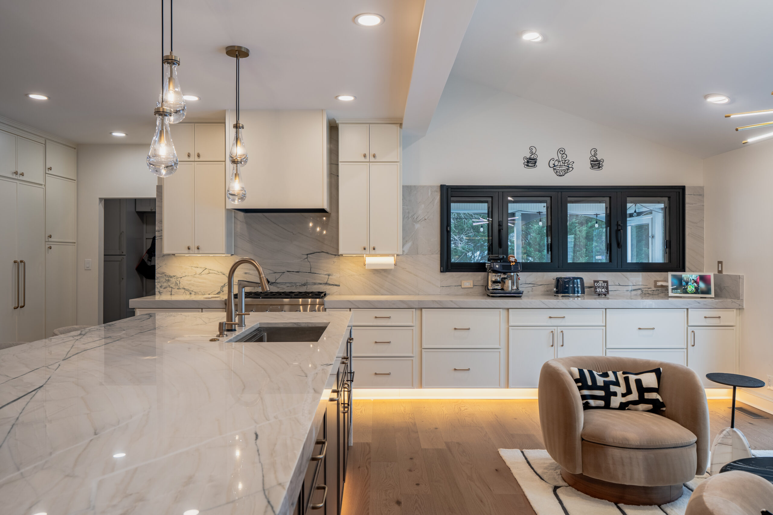 modern kitchen with marble countertops, white cabinets, under cabinet lighting, and lounge seating nearby