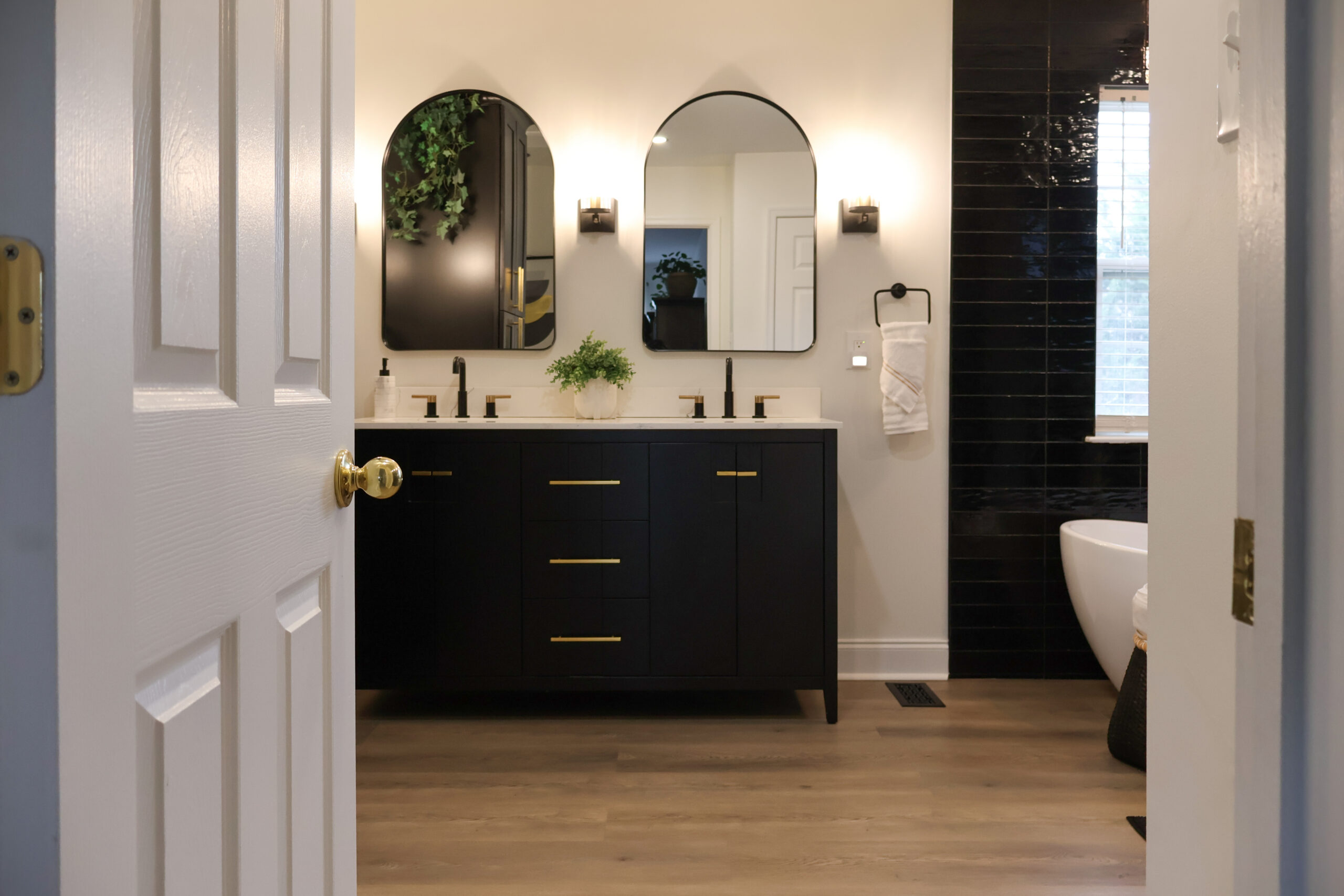 View through an open door of a renovated bathroom in Dupont Circle DC showing a black vanity and black tile accent wall.