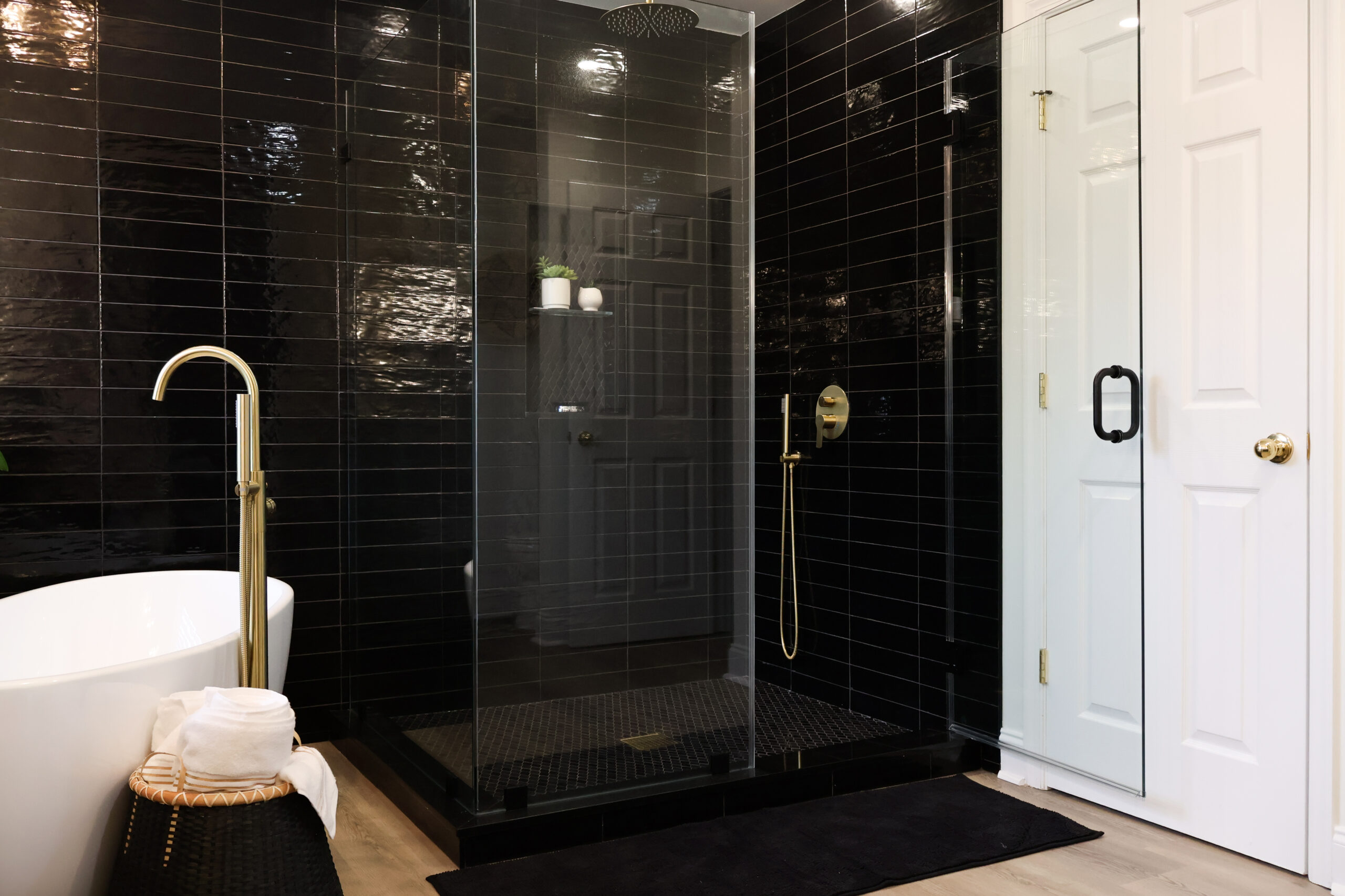 Glass-enclosed walk-in shower in Dupont Circle DC featuring black glossy subway tiles, gold showerhead, and gold hardware.