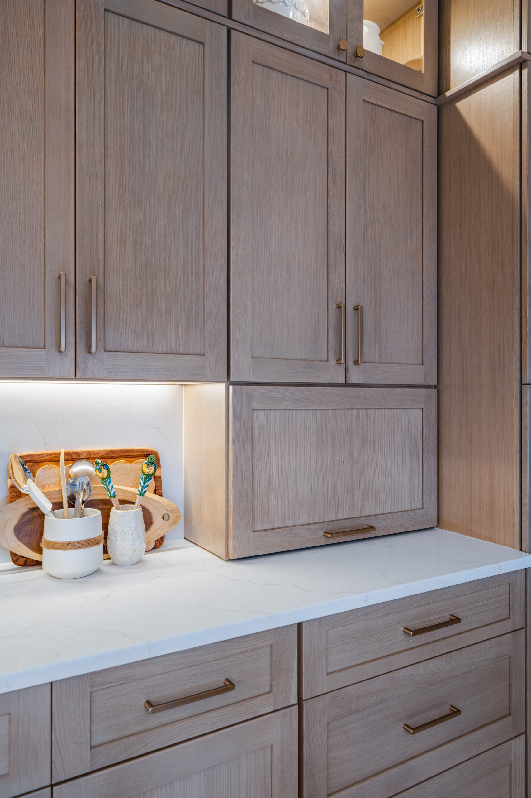 Close-up of a light wood appliance garage and custom drawers with slim brushed brass hardware.