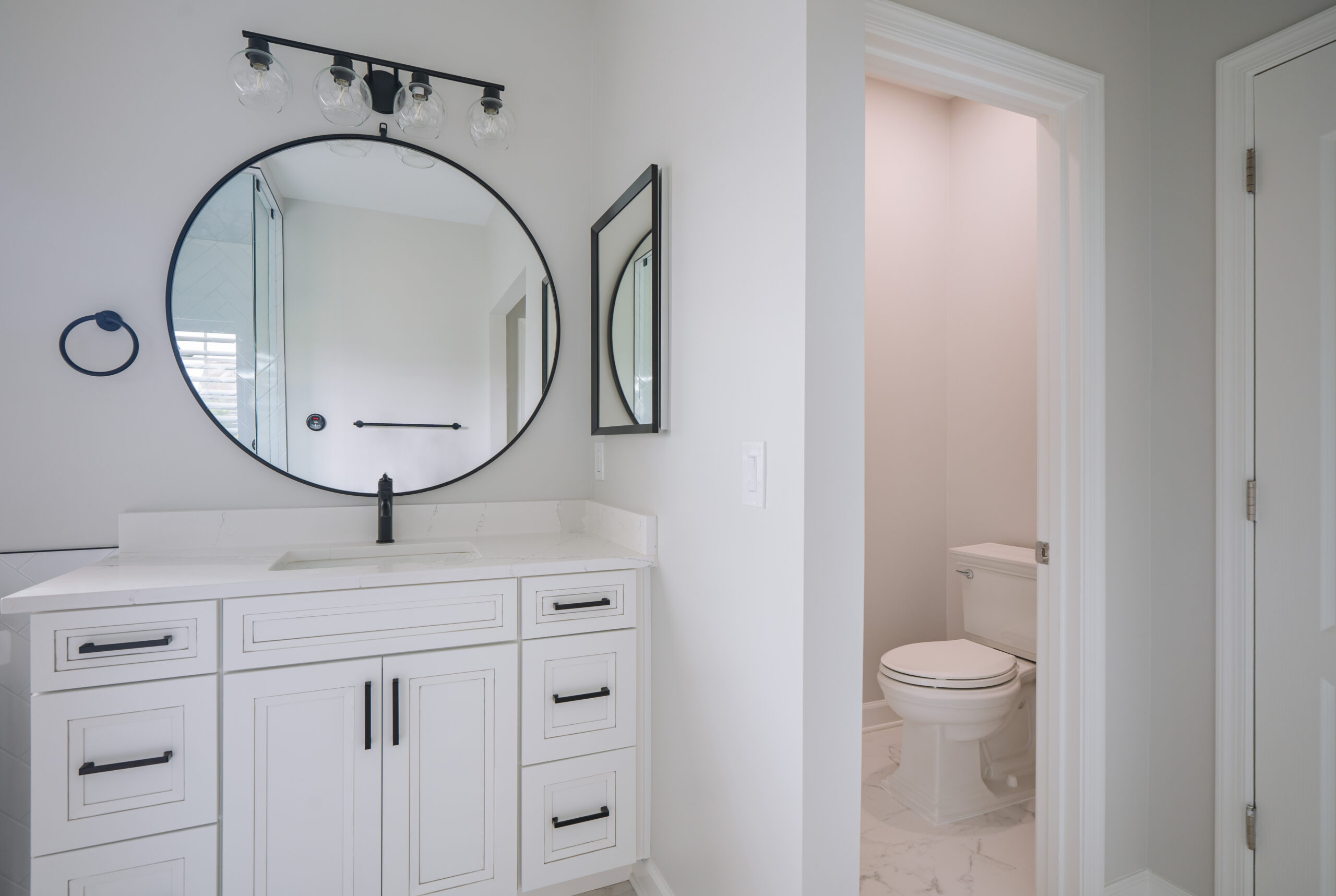 A white vanity area next to a private toilet room entrance in a remodeled bathroom.