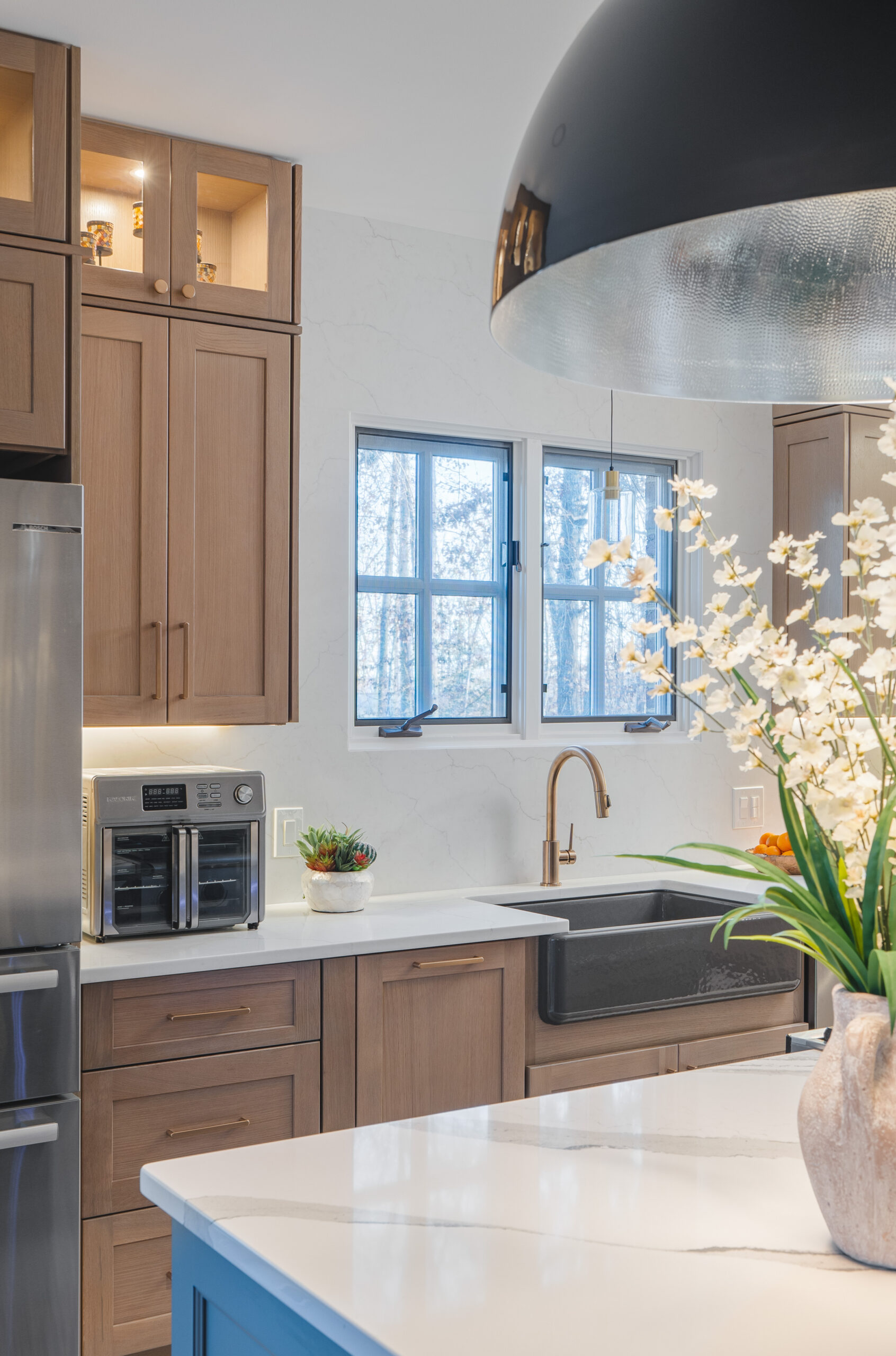 A matte black apron-front farmhouse sink paired with a brushed gold designer faucet and white quartz counters.