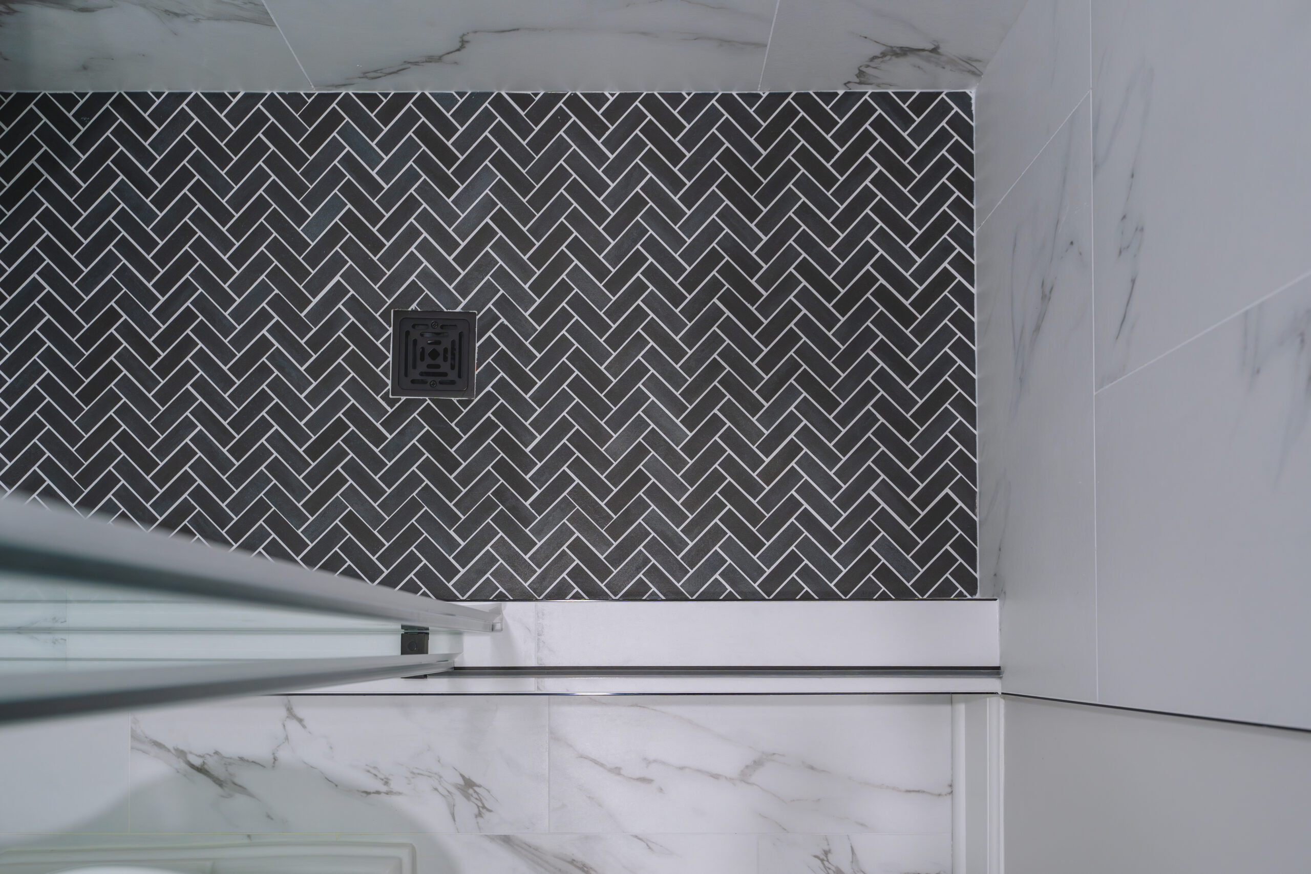 An overhead shot of black herringbone mosaic tiles on a shower floor with a square matte black drain.