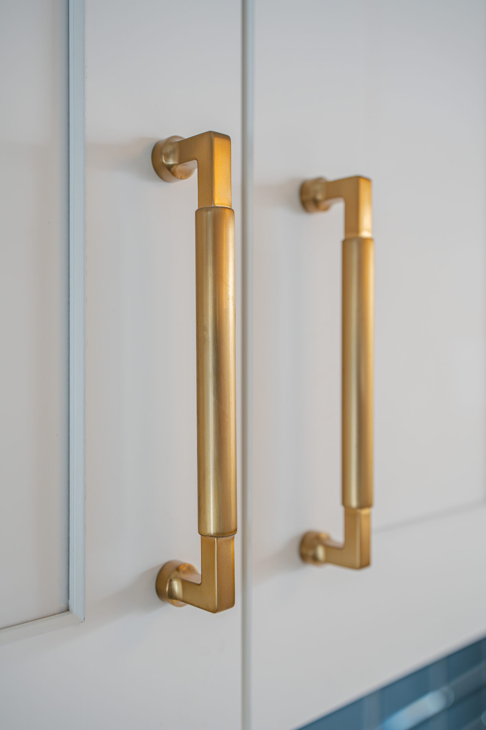 Close-up of vertical brushed gold handles on white shaker kitchen cabinets.