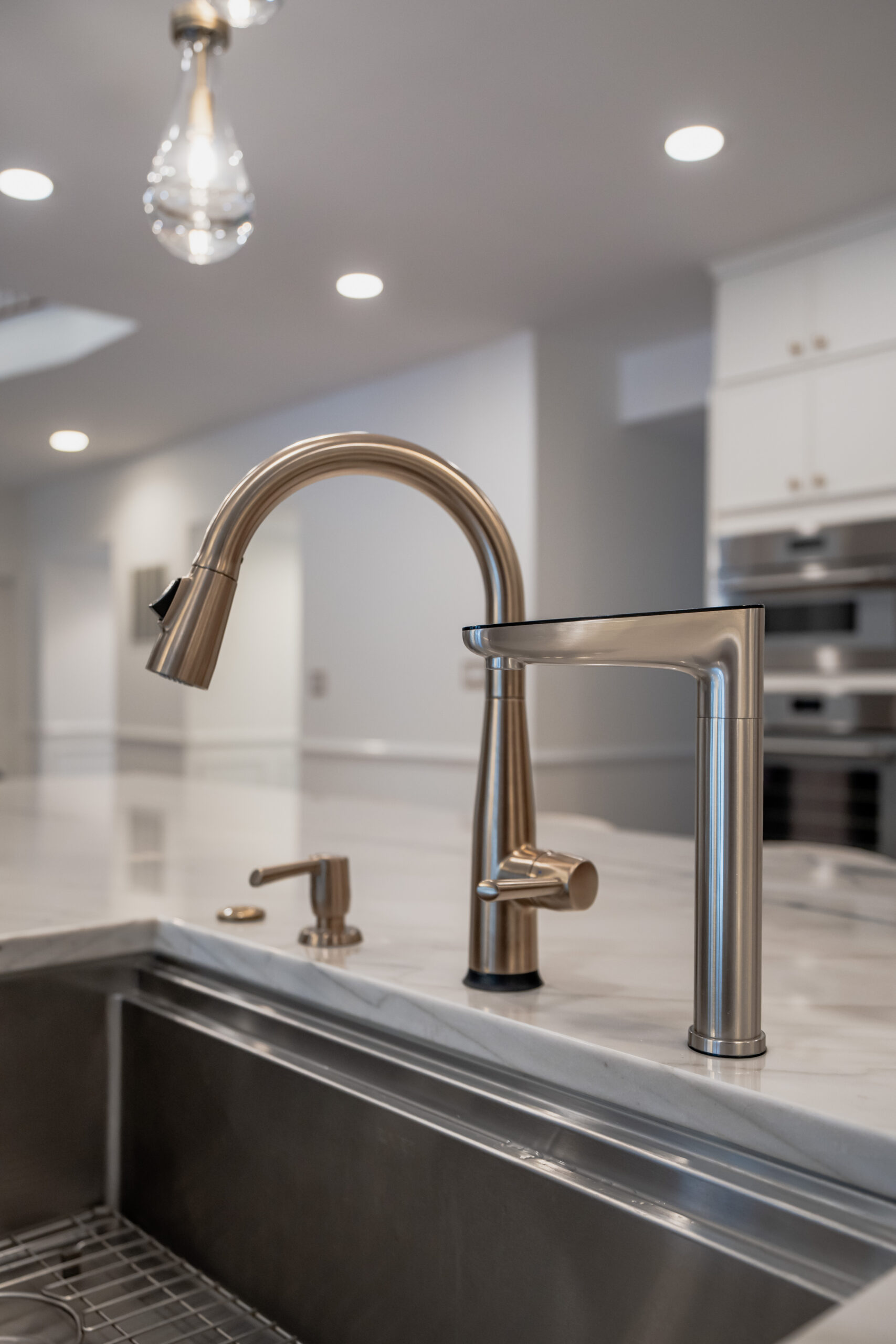 A brushed gold gooseneck kitchen faucet paired with a modern stainless steel water filtration dispenser on a marble countertop.