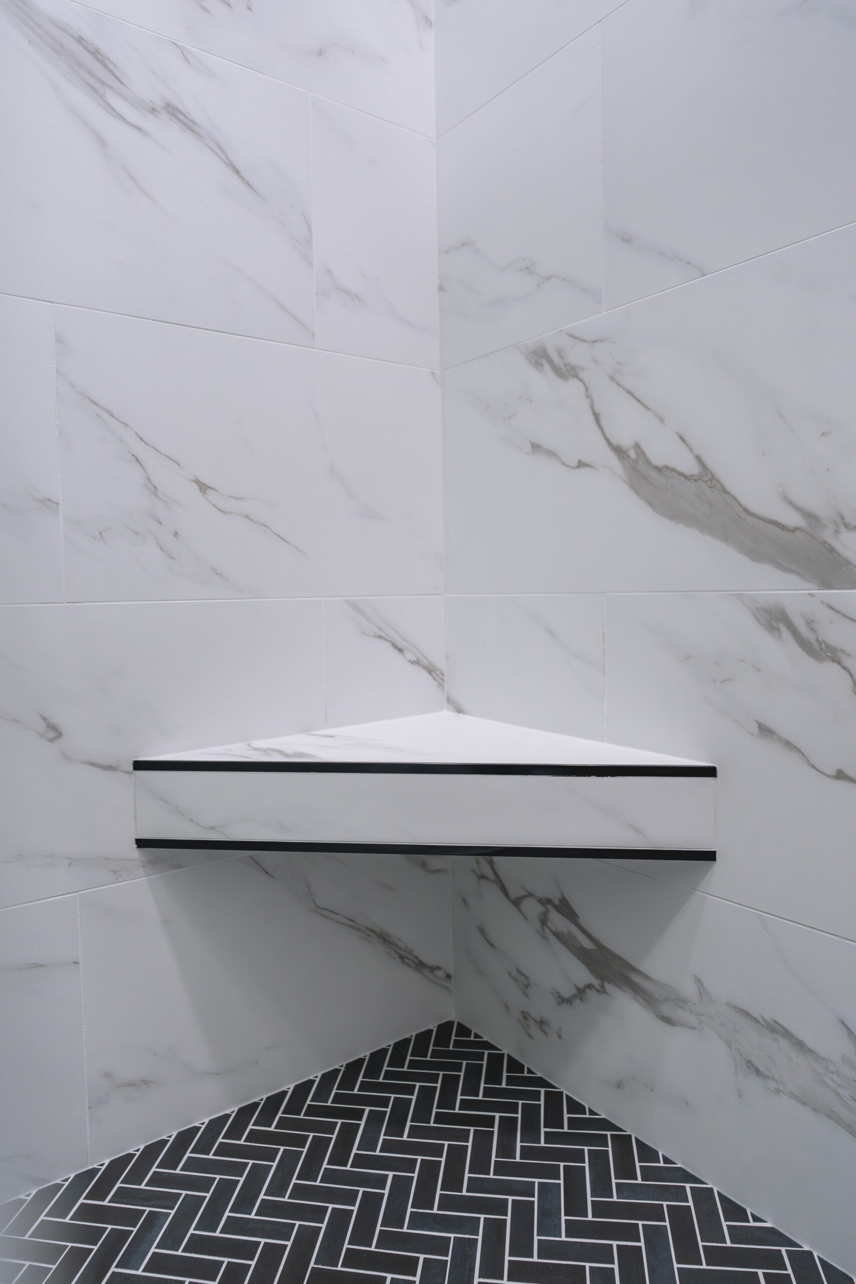 A corner-mounted white marble shower bench above a black herringbone tile floor.