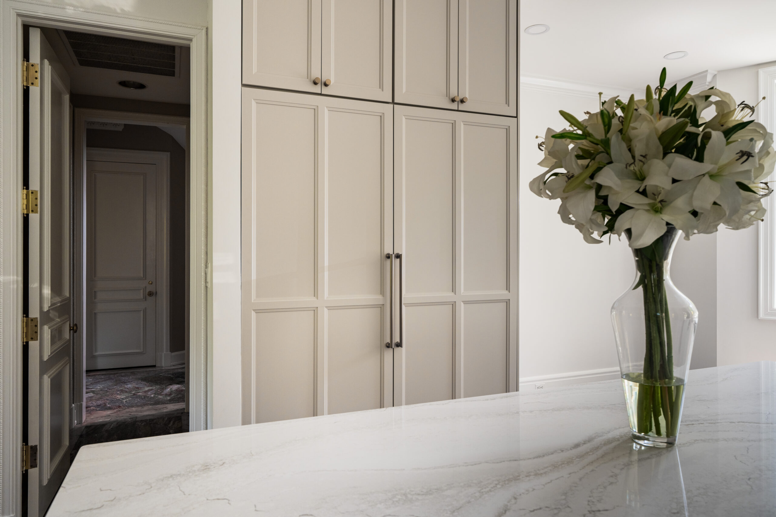 Floor-to-ceiling modern pantry cabinets with slim gold handles located next to a kitchen walkway.