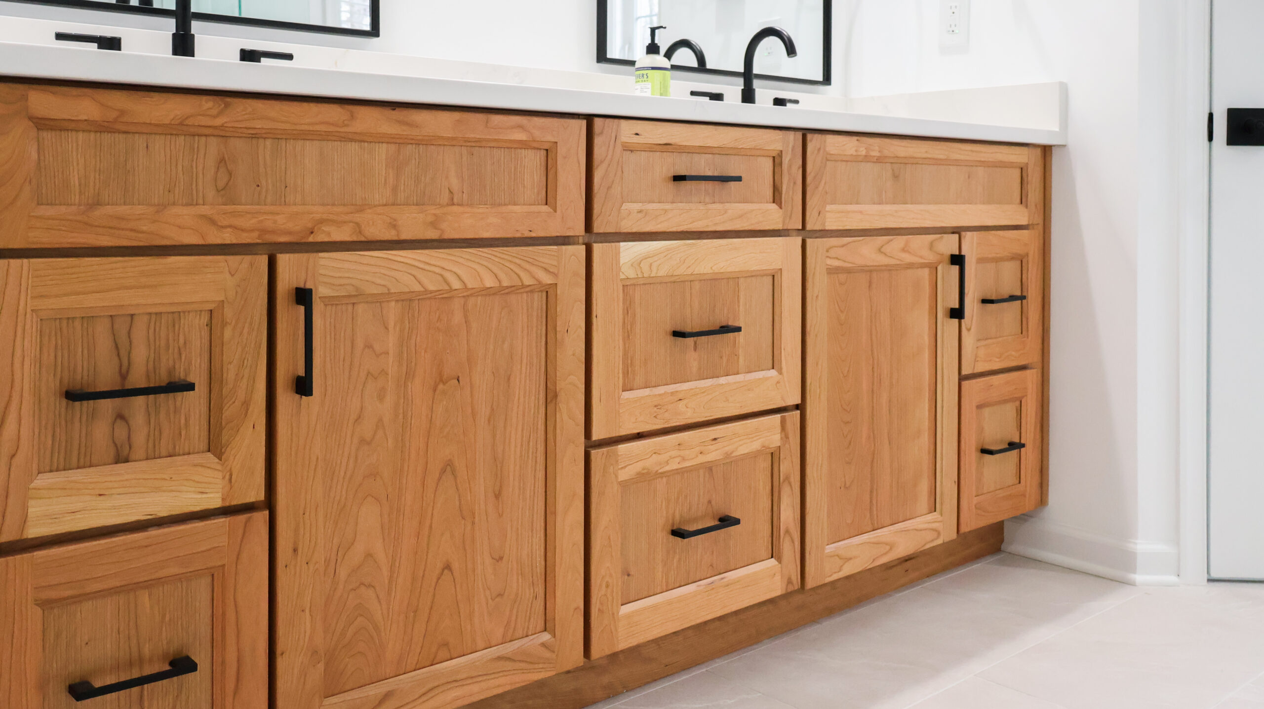Close up of natural light wood bathroom cabinet drawers with modern matte black handles and pulls.