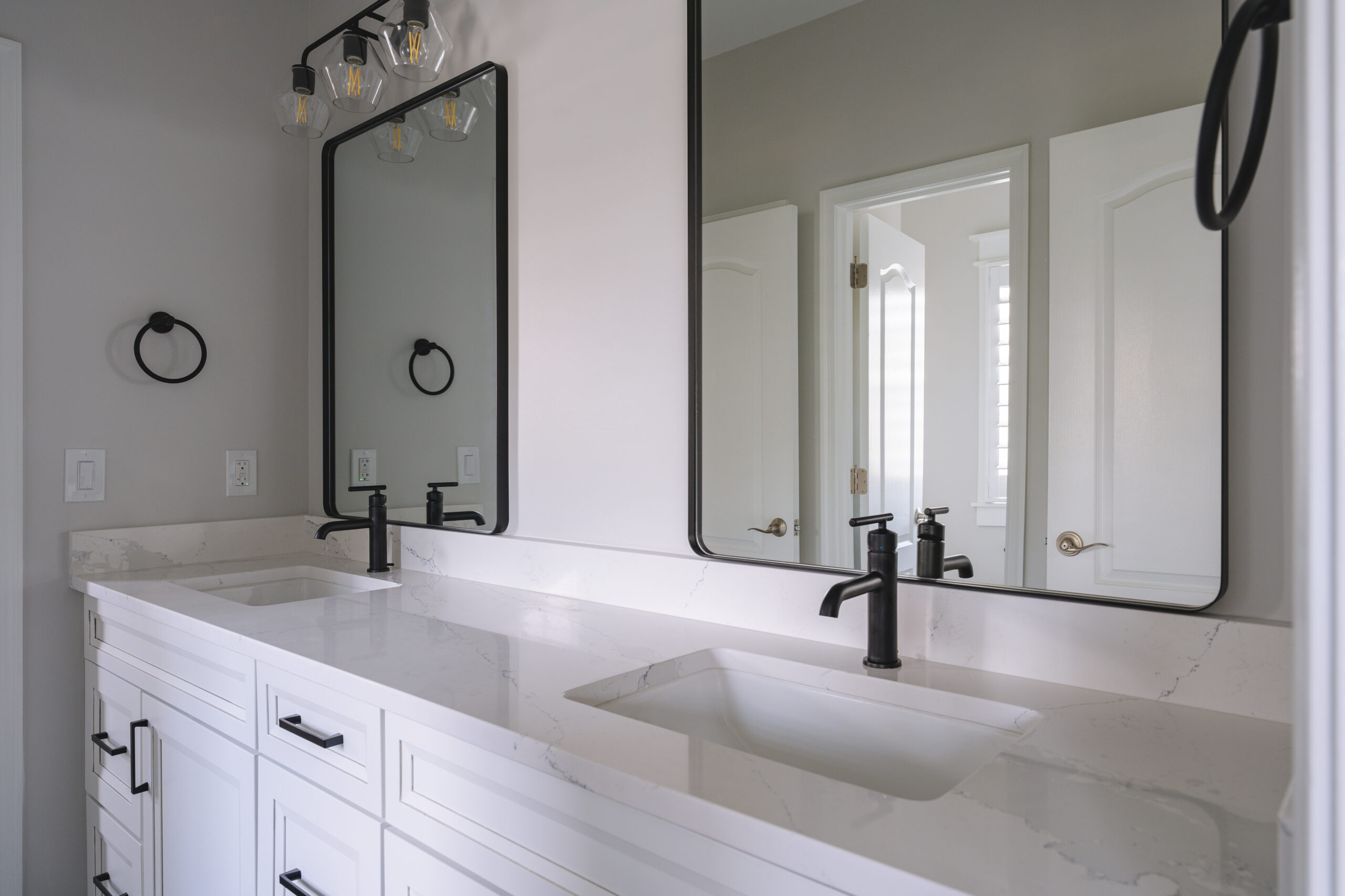 White double vanity featuring rectangular black-framed mirrors and matte black faucets.