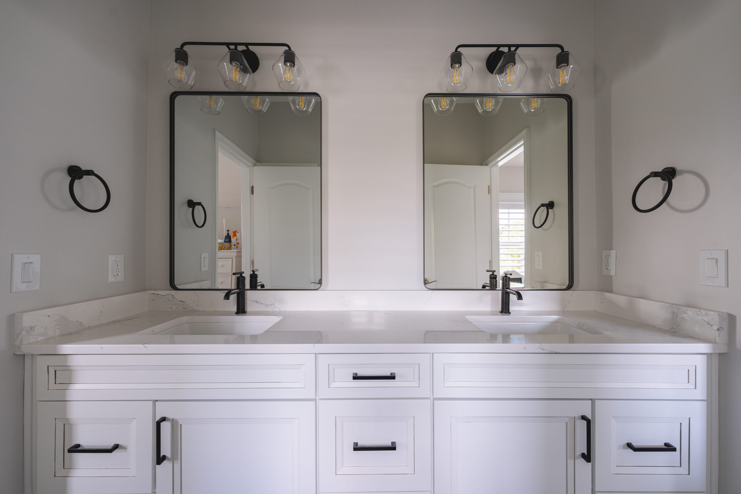 A frontal view of a white double vanity with two rectangular black-framed mirrors and modern globe lighting fixtures.