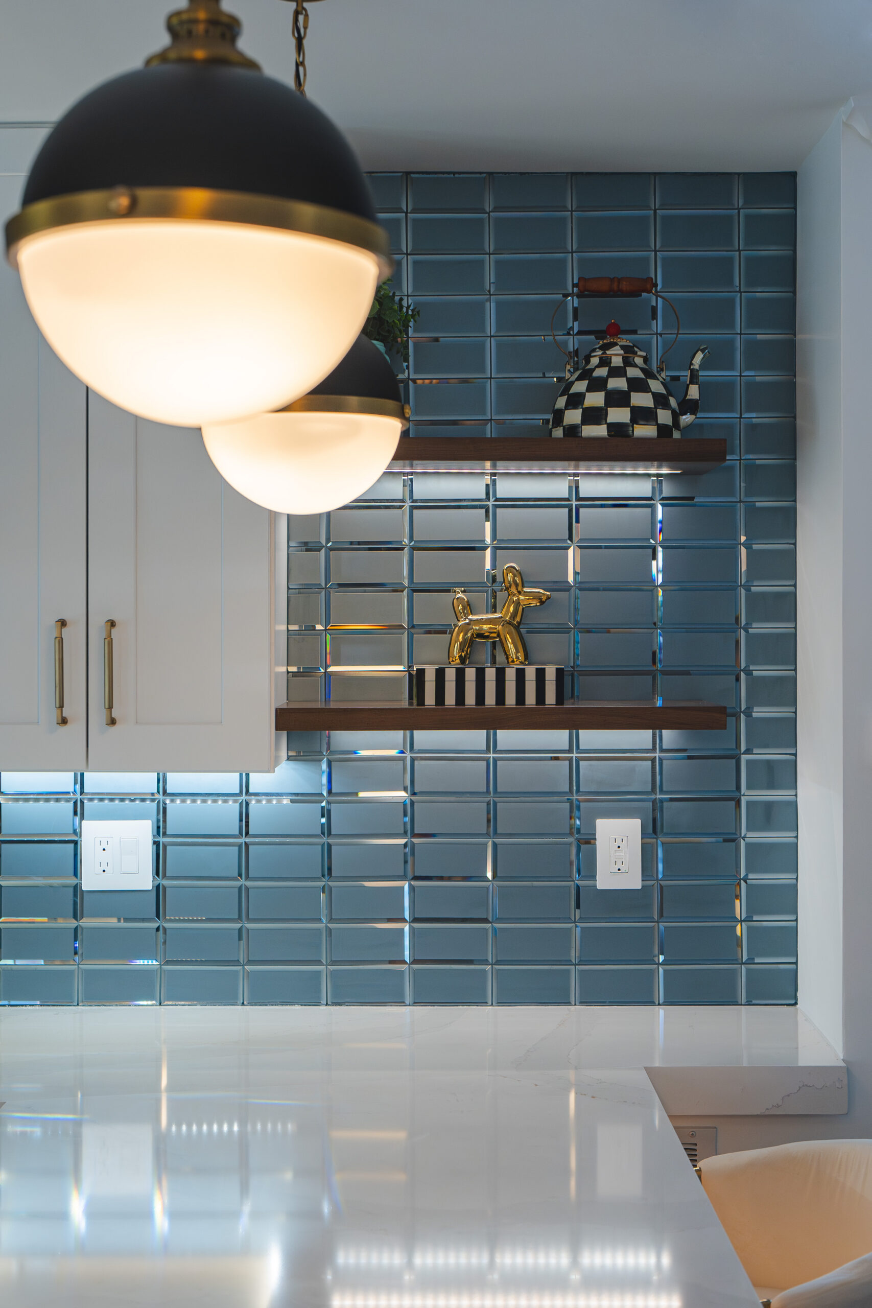 Dark wood floating shelves mounted on a teal glass subway tile backsplash with decorative gold accents.