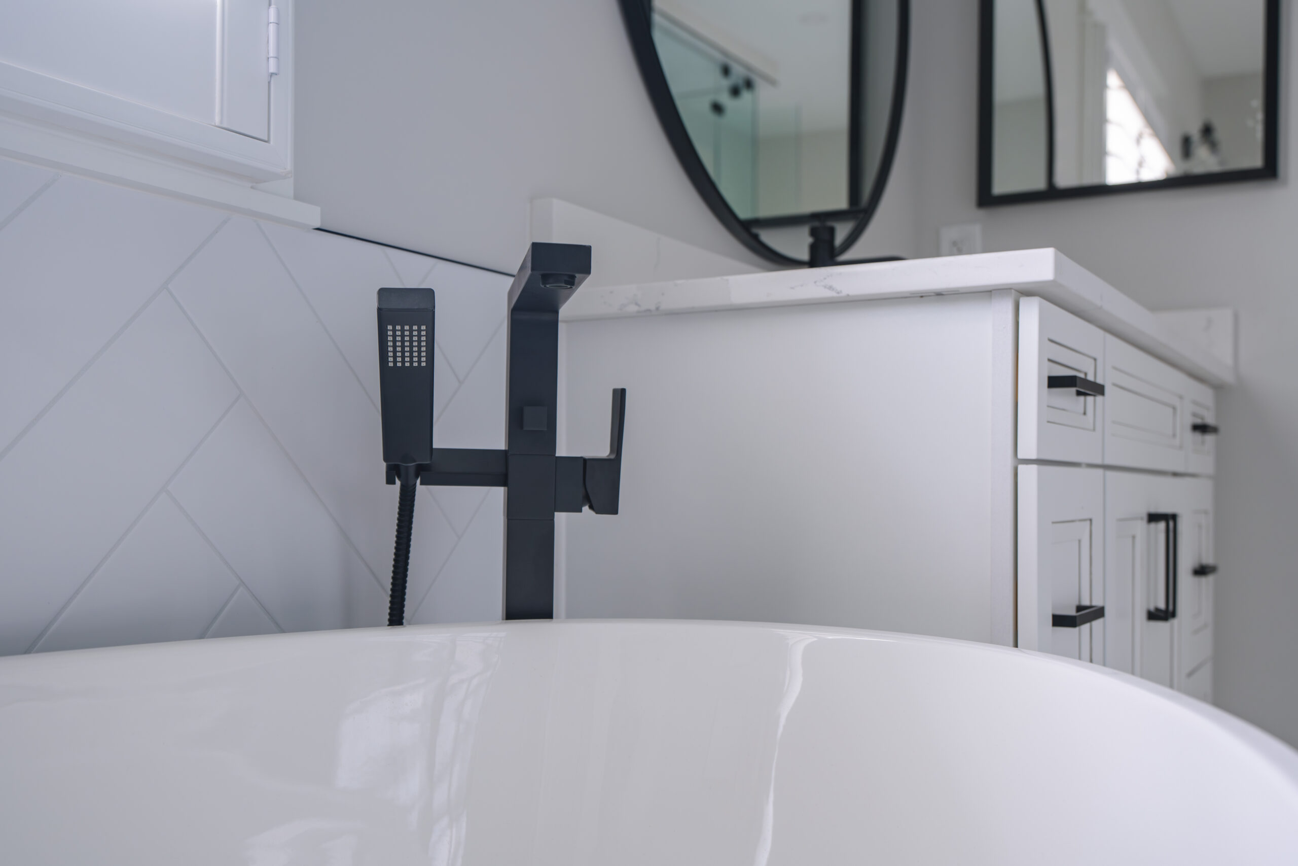 A side view of a matte black floor-mounted faucet next to a white freestanding tub.