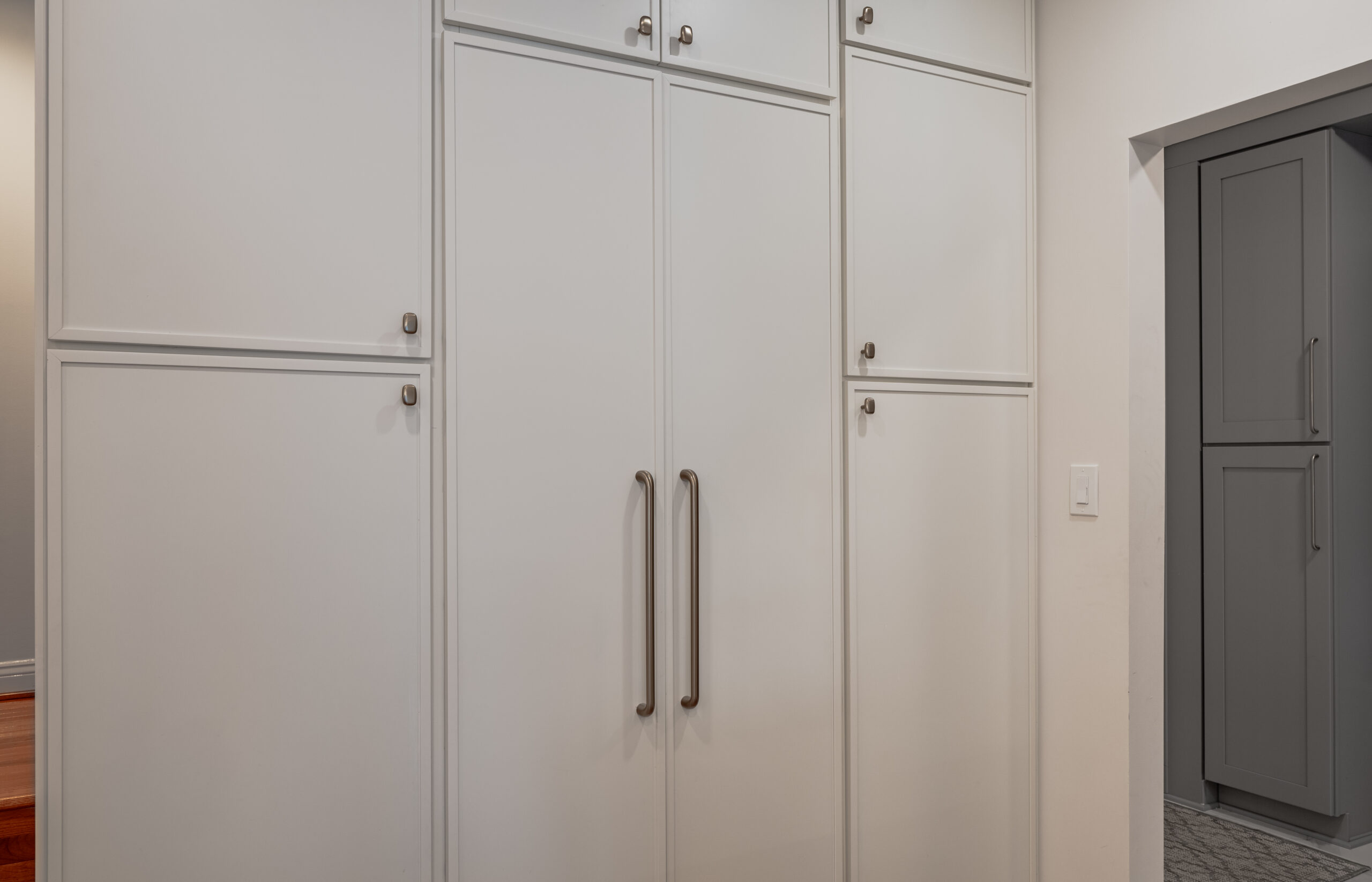 A wall of floor-to-ceiling white kitchen storage cabinets with long gold pull handles.