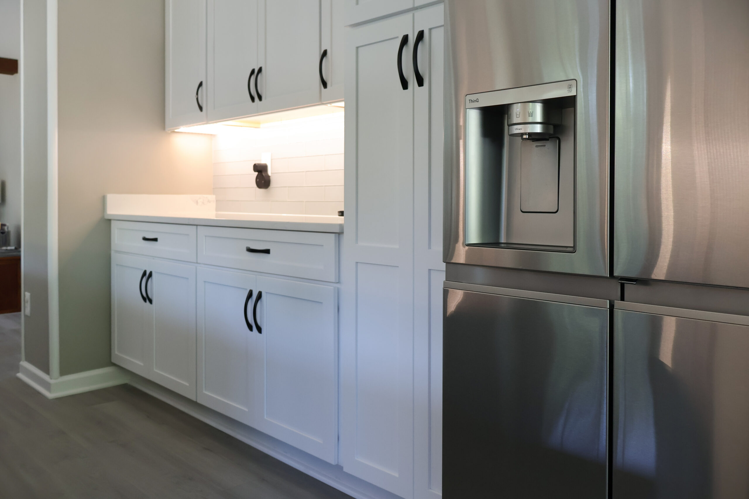 Floor to ceiling white shaker pantry cabinets next to a stainless refrigerator.