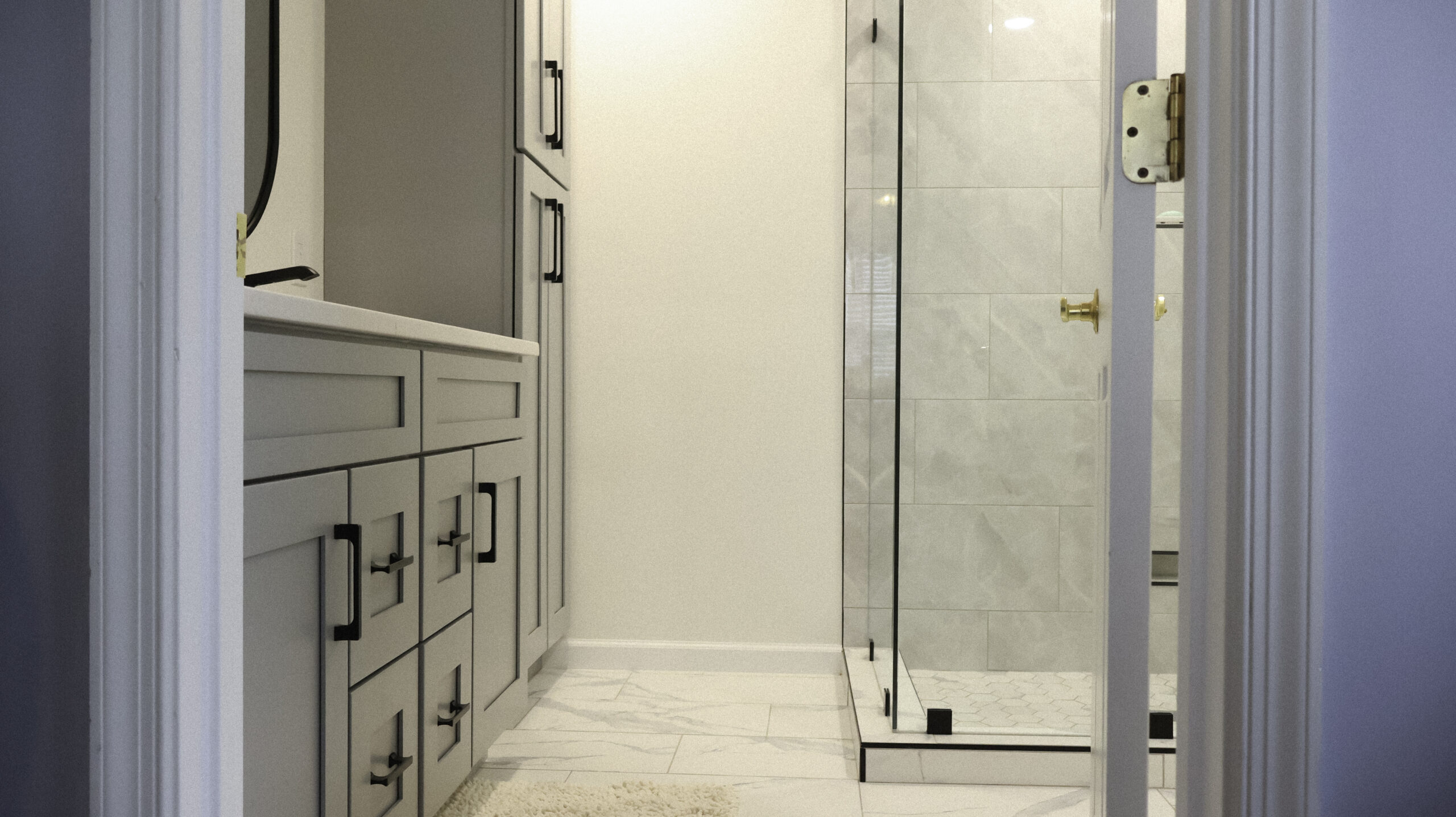View of a frameless glass shower enclosure and custom gray cabinetry