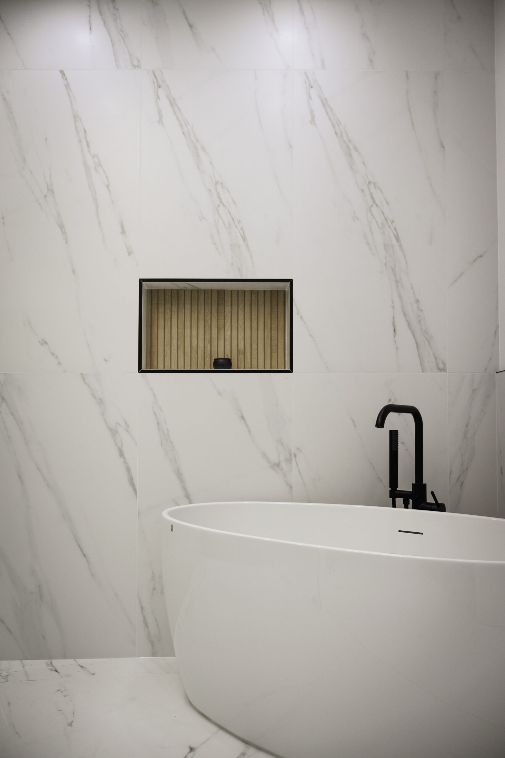 White soaking tub with matte black wall-mounted faucet.