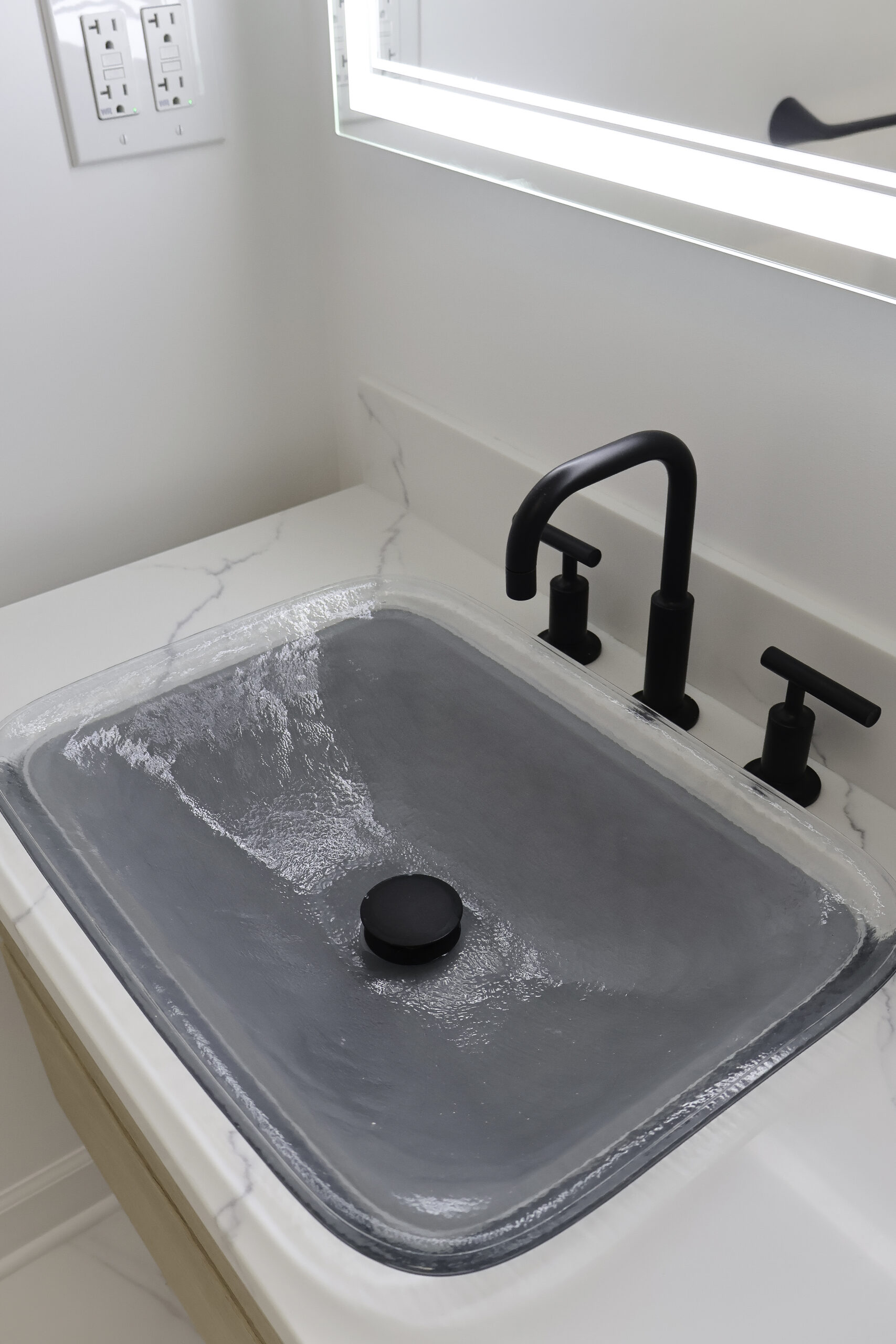 Close up of a glass vessel sink and matte black gooseneck faucet.