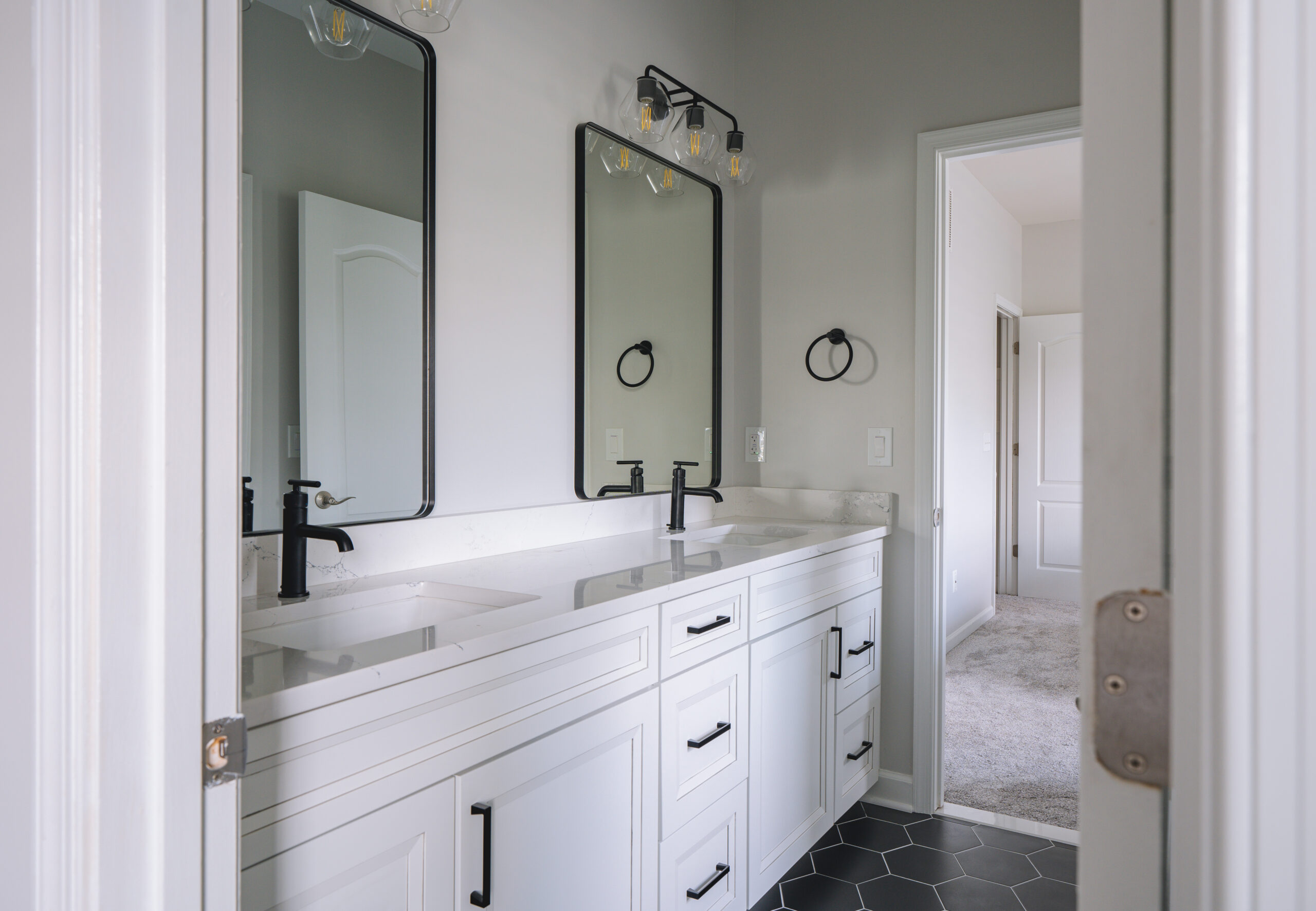 A white bathroom vanity with black hardware and rectangular black mirrors over a black hexagon tile floor.