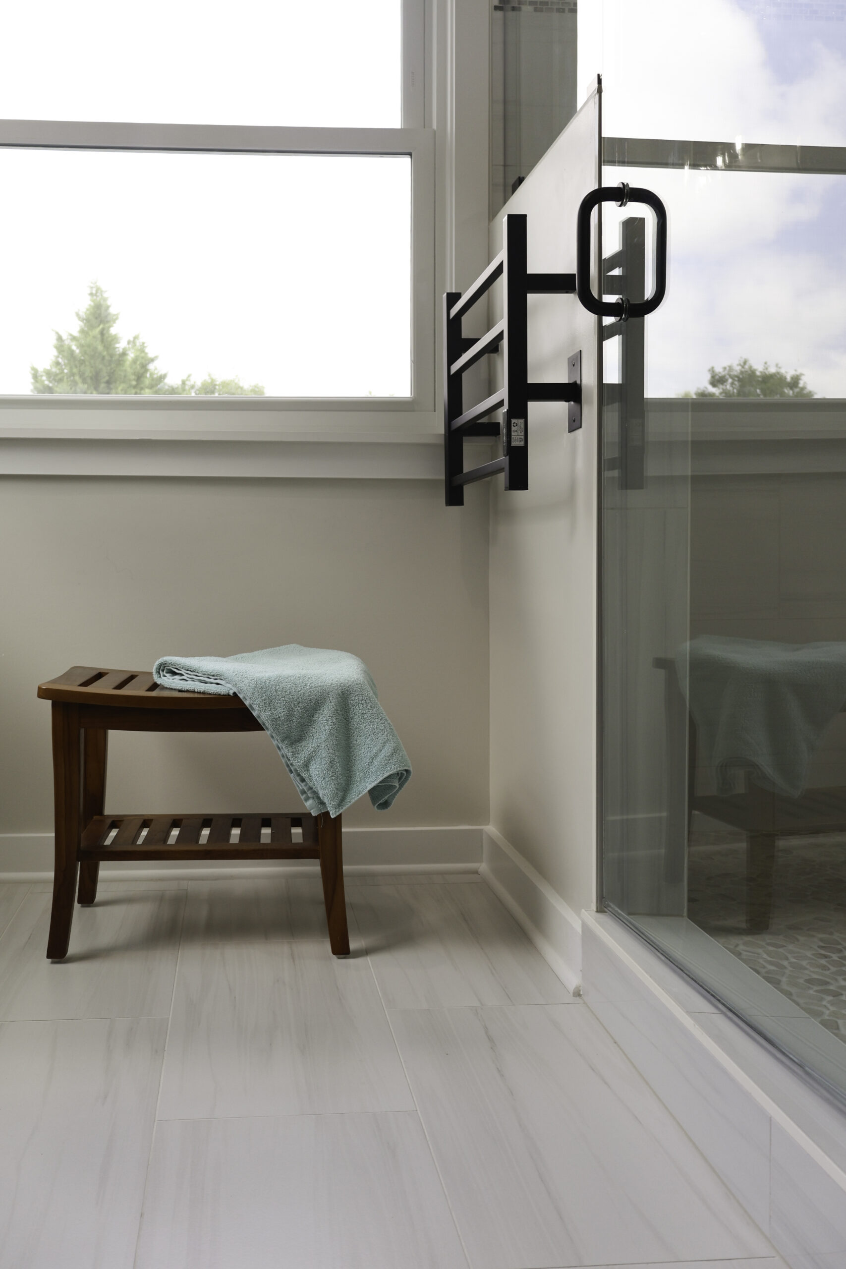 Wall mounted black heated towel rack next to a wooden shower bench.