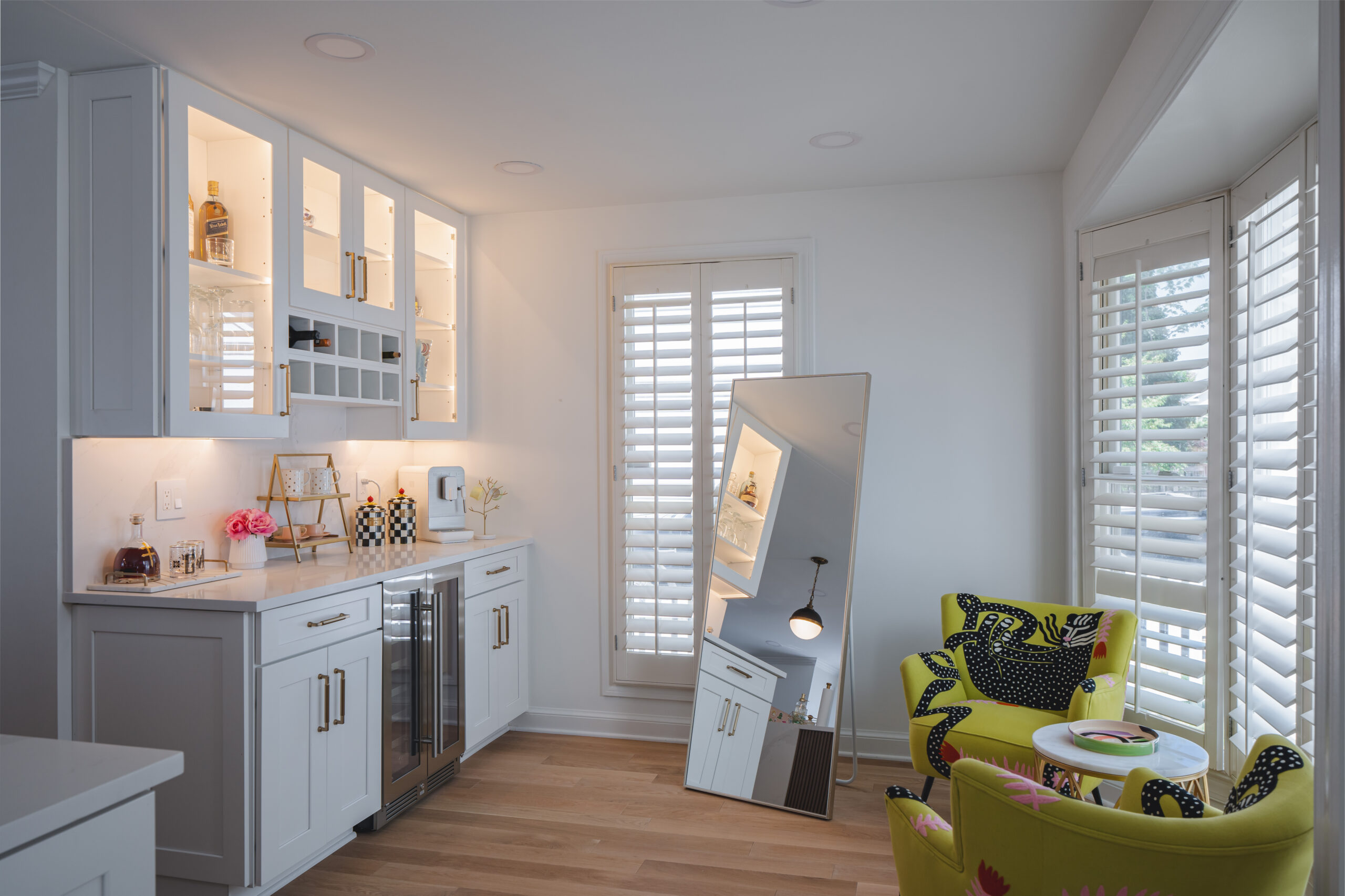 A dedicated kitchen bar area with lit glass-front cabinets, a wine fridge, and stylish chartreuse accent chairs.
