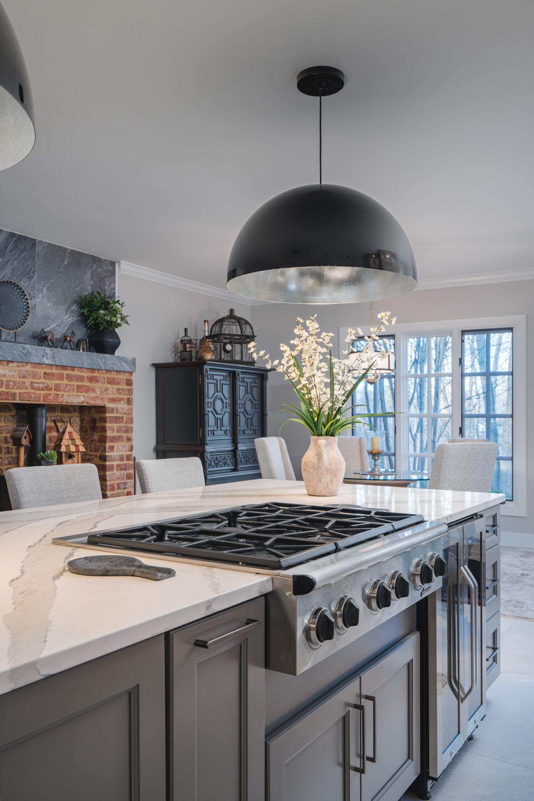 View from a modern kitchen island looking into a living room with a brick fireplace and breakfast nook.