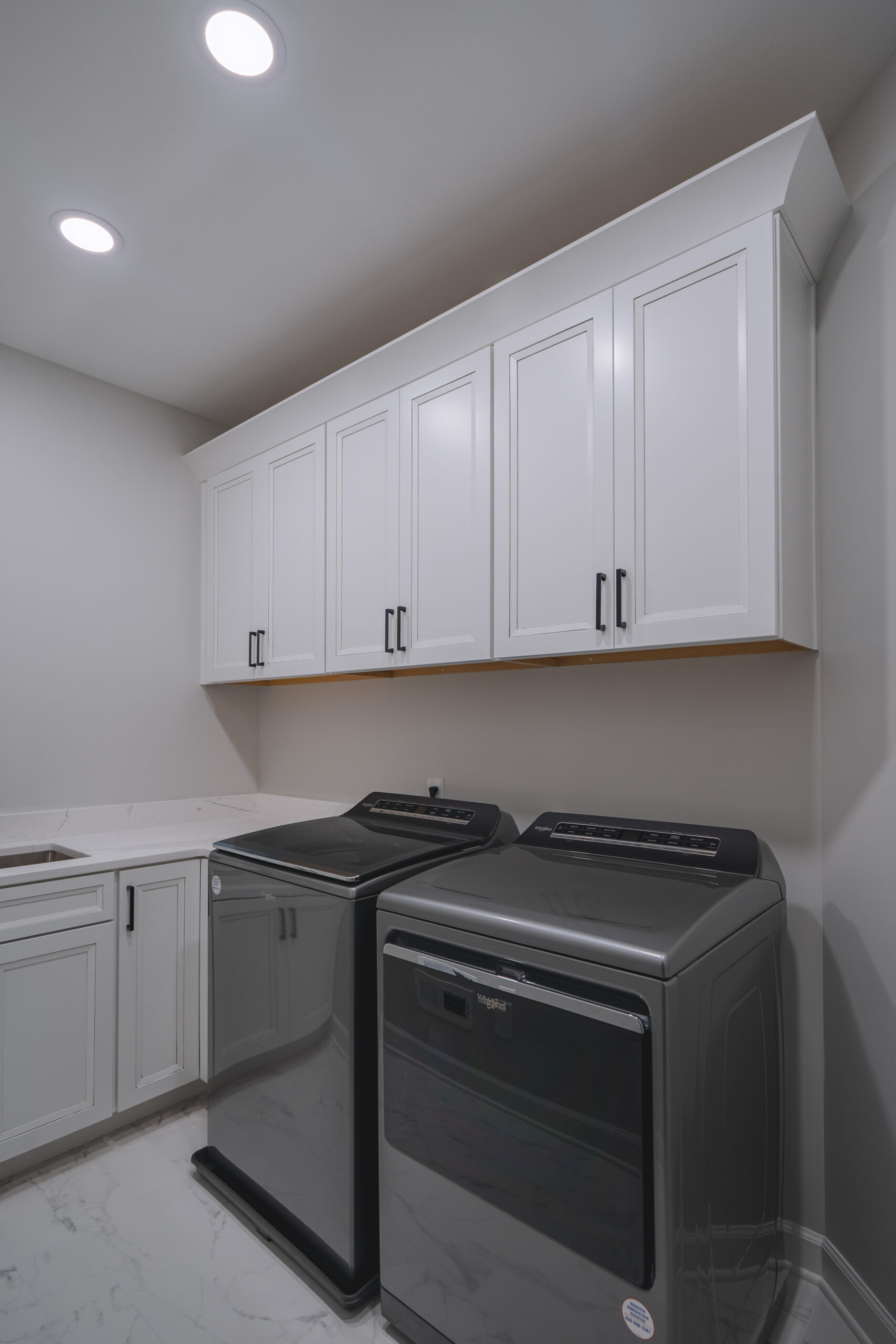 White upper laundry room cabinets with black handles installed above a gray high-efficiency washer and dryer set.