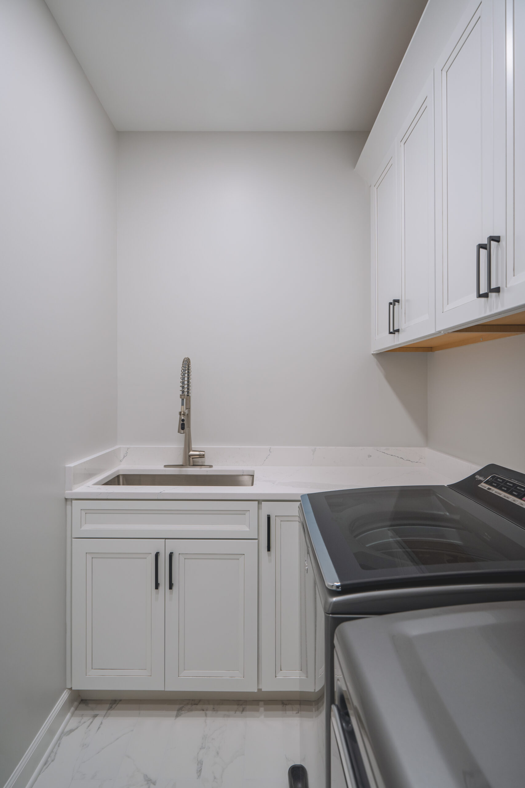 A stainless steel undermount utility sink with a high-arc faucet set into a white marble-look quartz countertop.