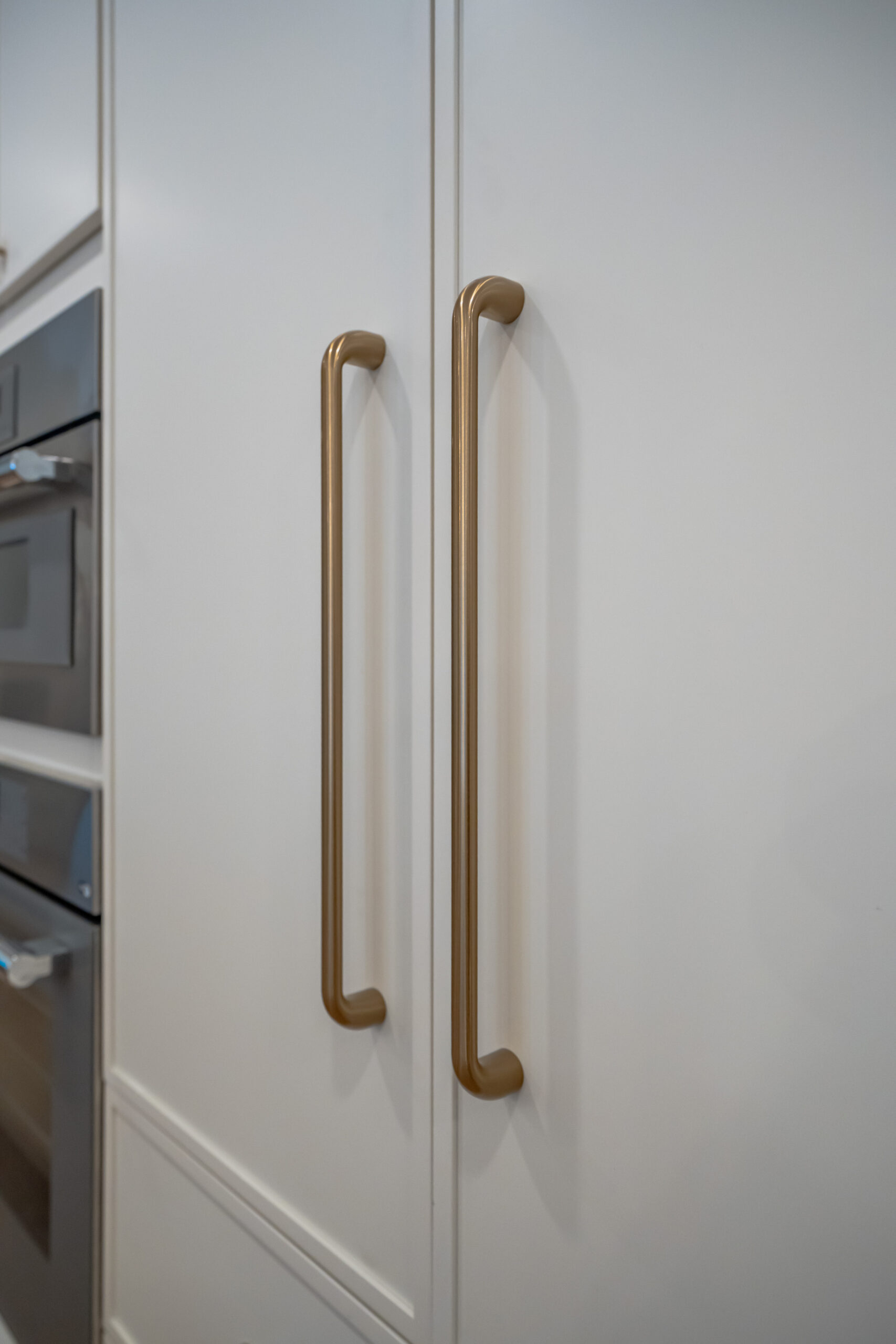 Detailed shot of long, slim brushed gold handles installed on custom floor-to-ceiling white kitchen pantry cabinets.