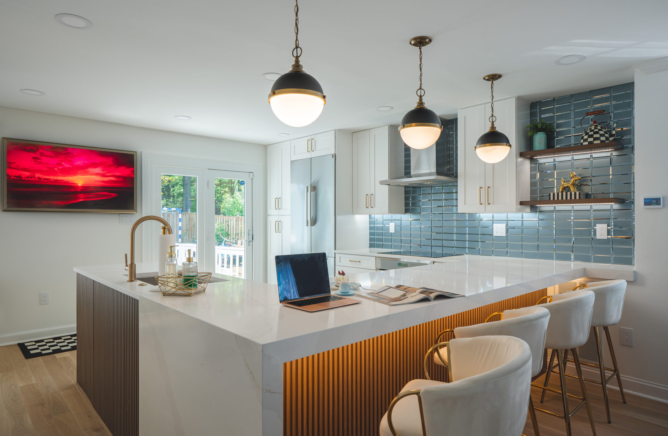 A wide view of a bright kitchen with a large central island, white cabinetry, and a vibrant teal glass tile backsplash.