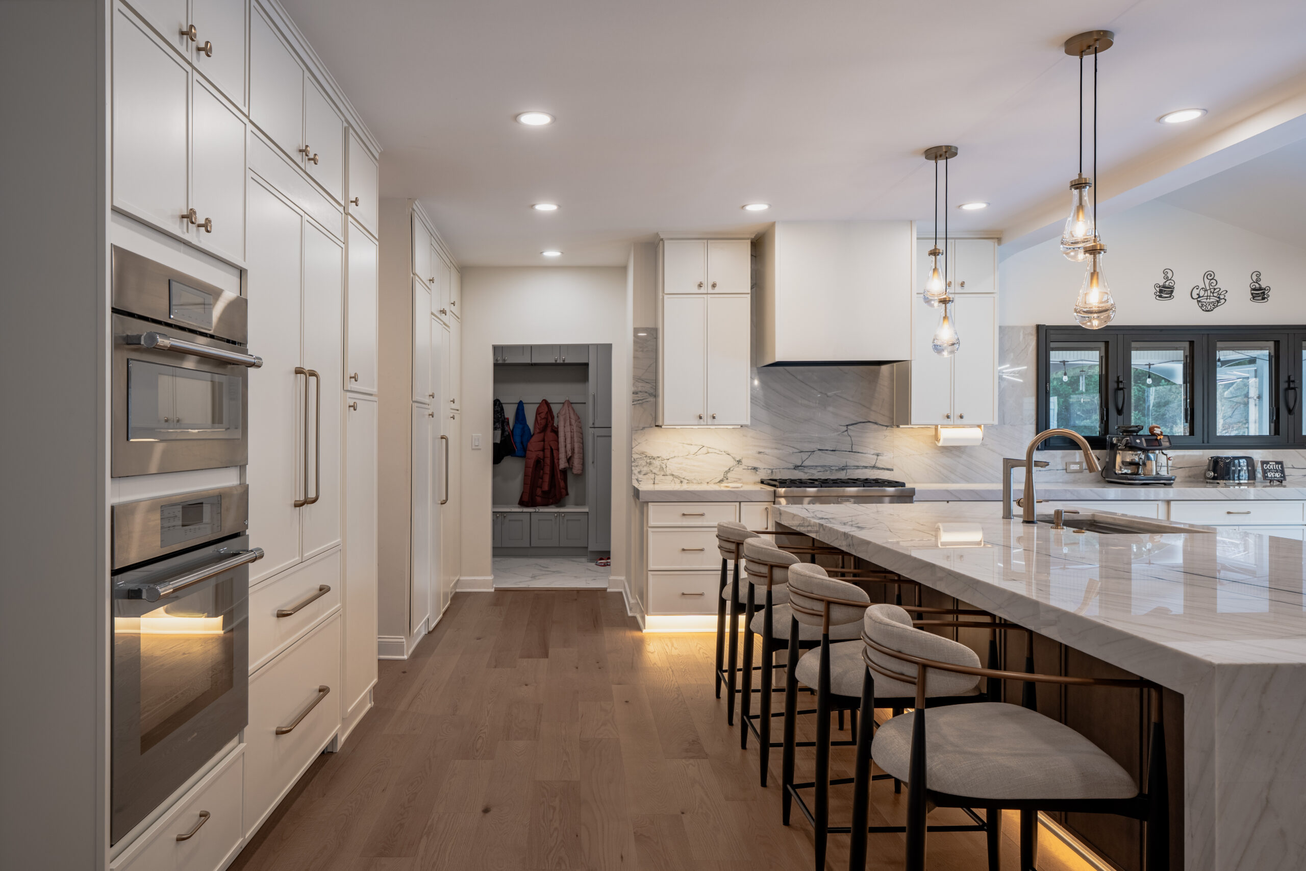 A view of floor-to-ceiling white kitchen cabinets with integrated stainless steel Thermador double ovens and gold hardware.