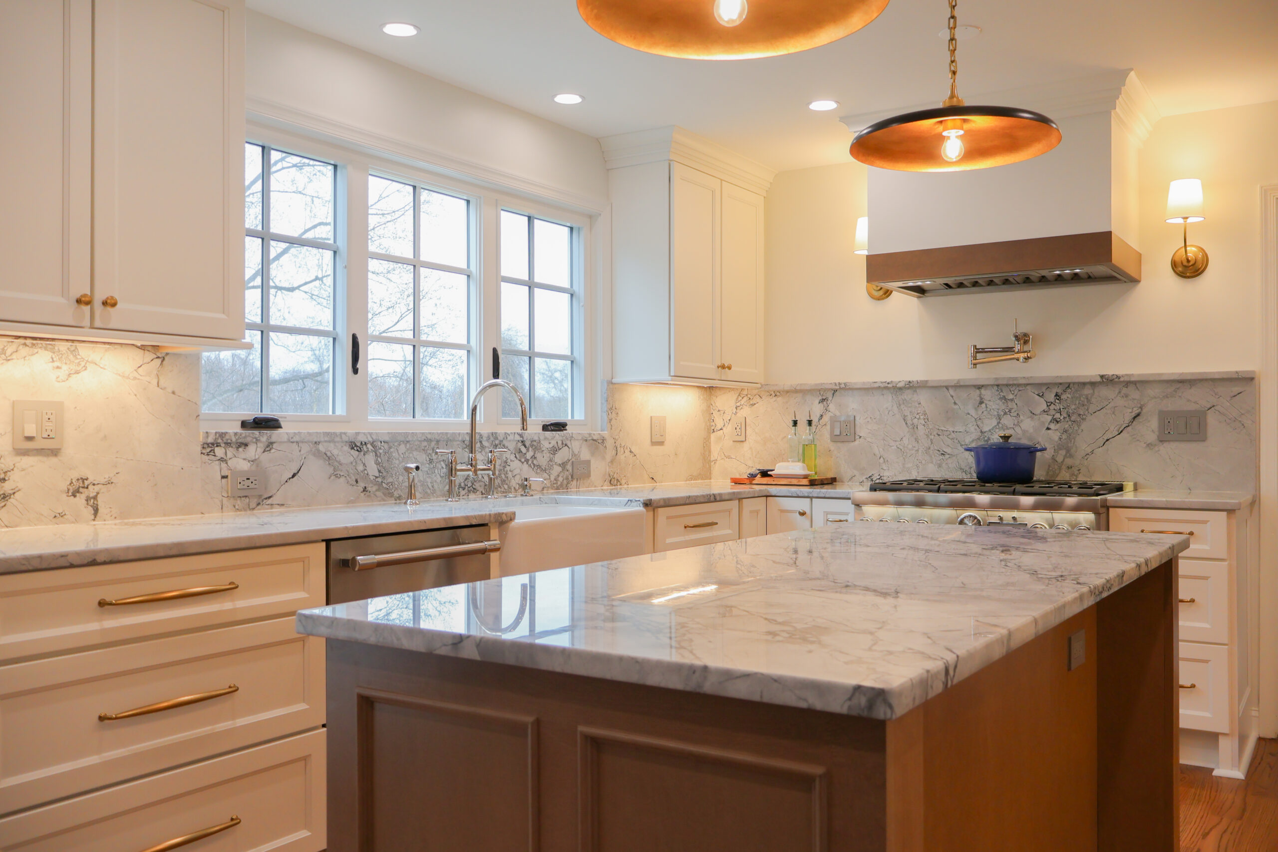 A large Georgetown DC kitchen island with a thick marble top and two large black and brass saucer-style pendant lights.