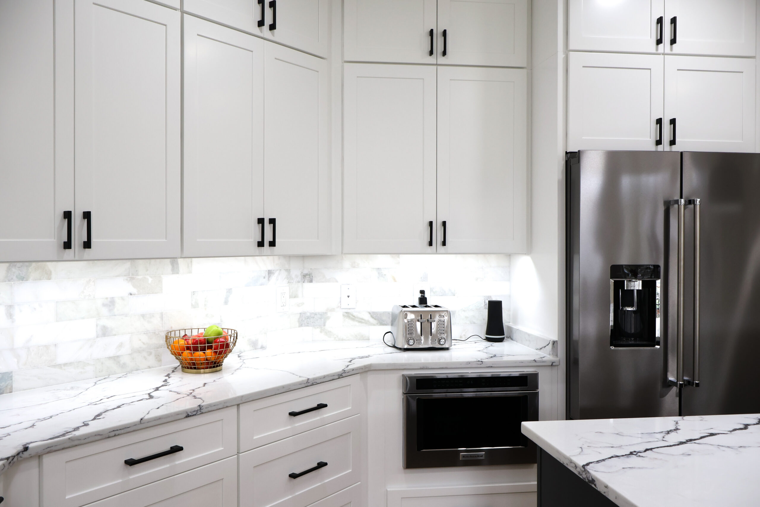 Modern kitchen setup featuring marble subway tile and an integrated stainless microwave drawer.
