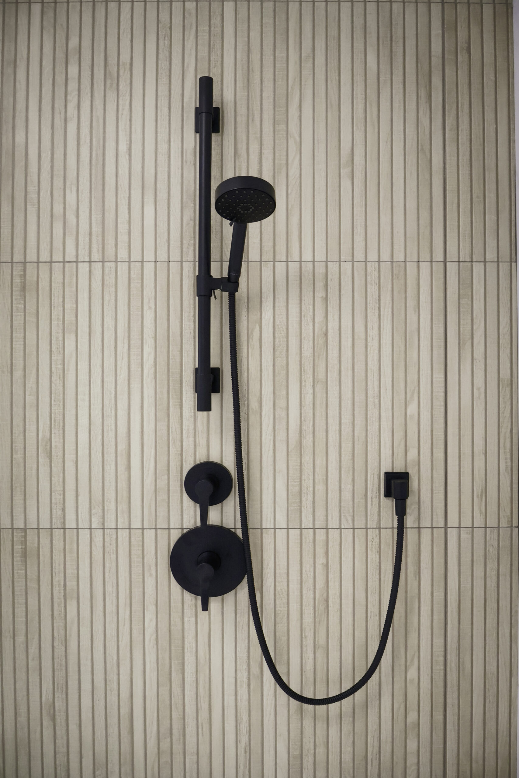 Close up of matte black shower controls mounted on vertical wood slat tile.