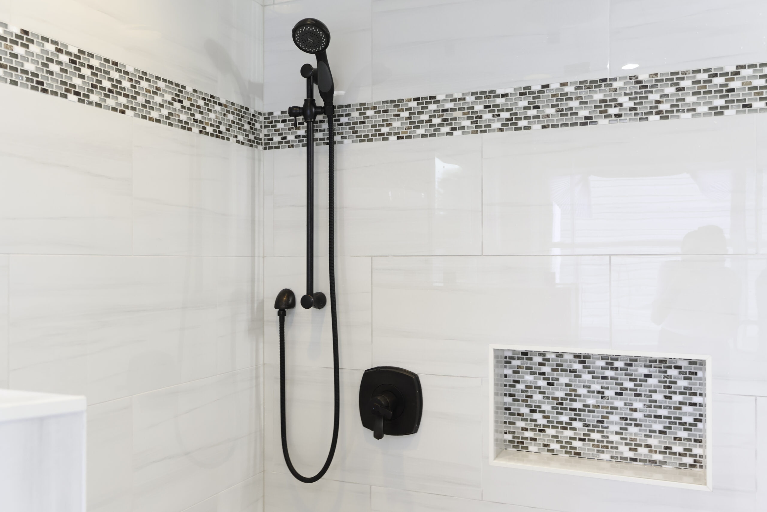 Matte black shower fixtures and mosaic tile border detail.