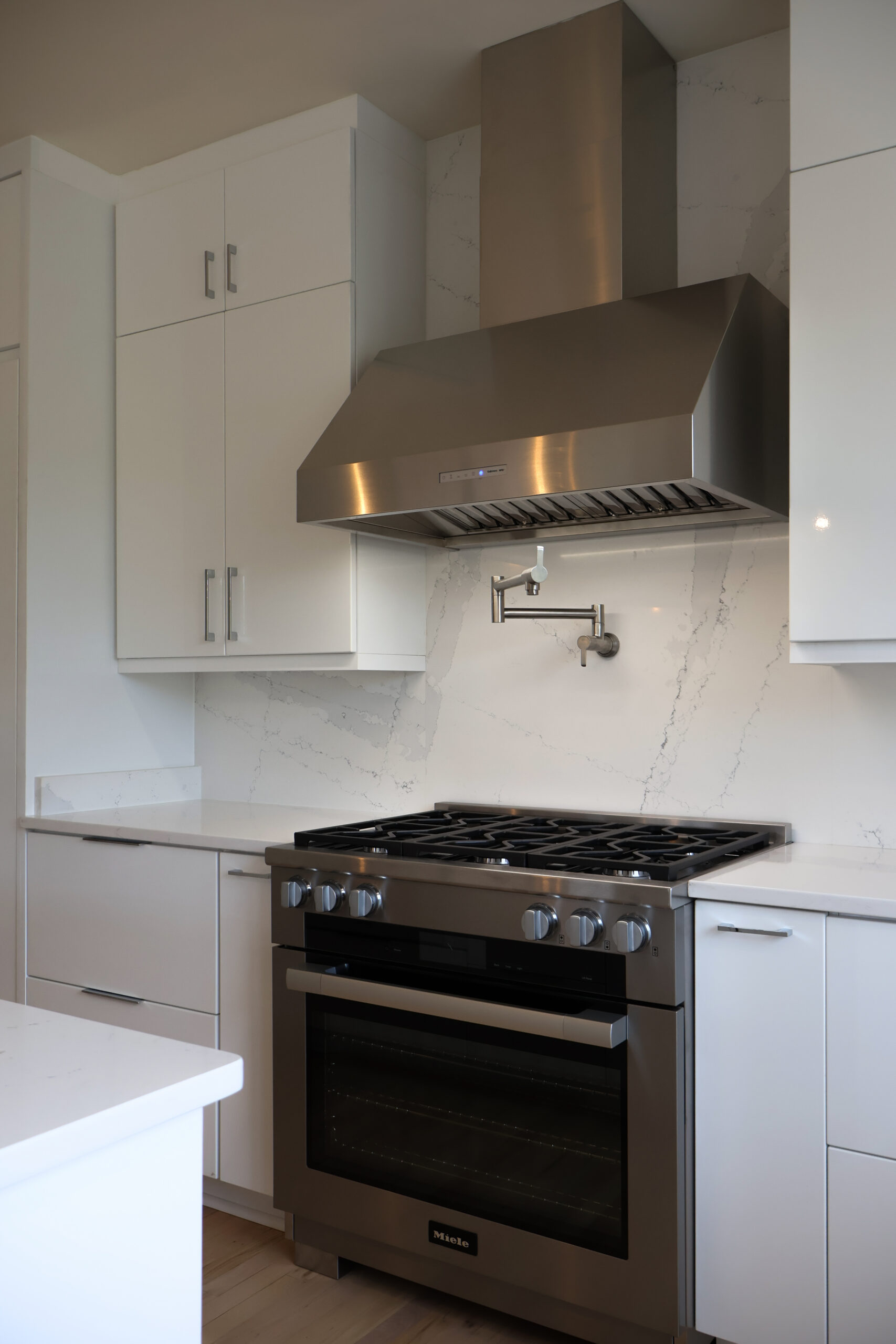 Close up of a Miele professional gas range and stainless steel ventilation hood.