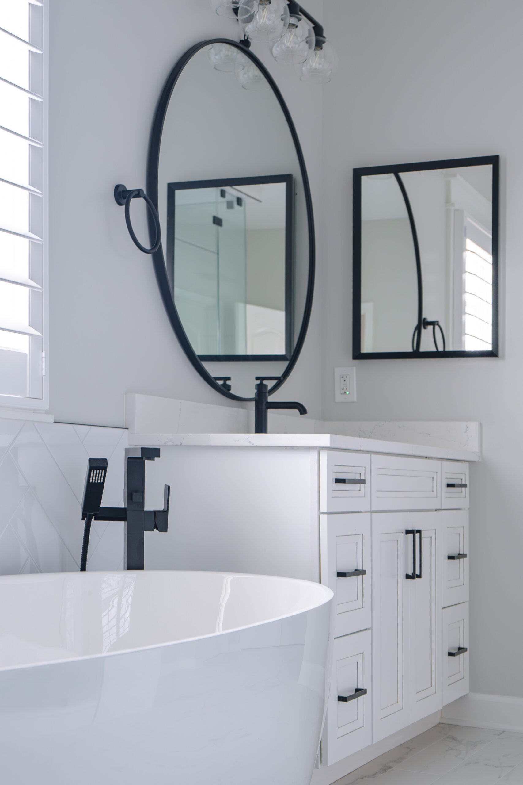 A low-angle shot showing a white bathroom vanity with black hardware next to the edge of a white soaking tub.