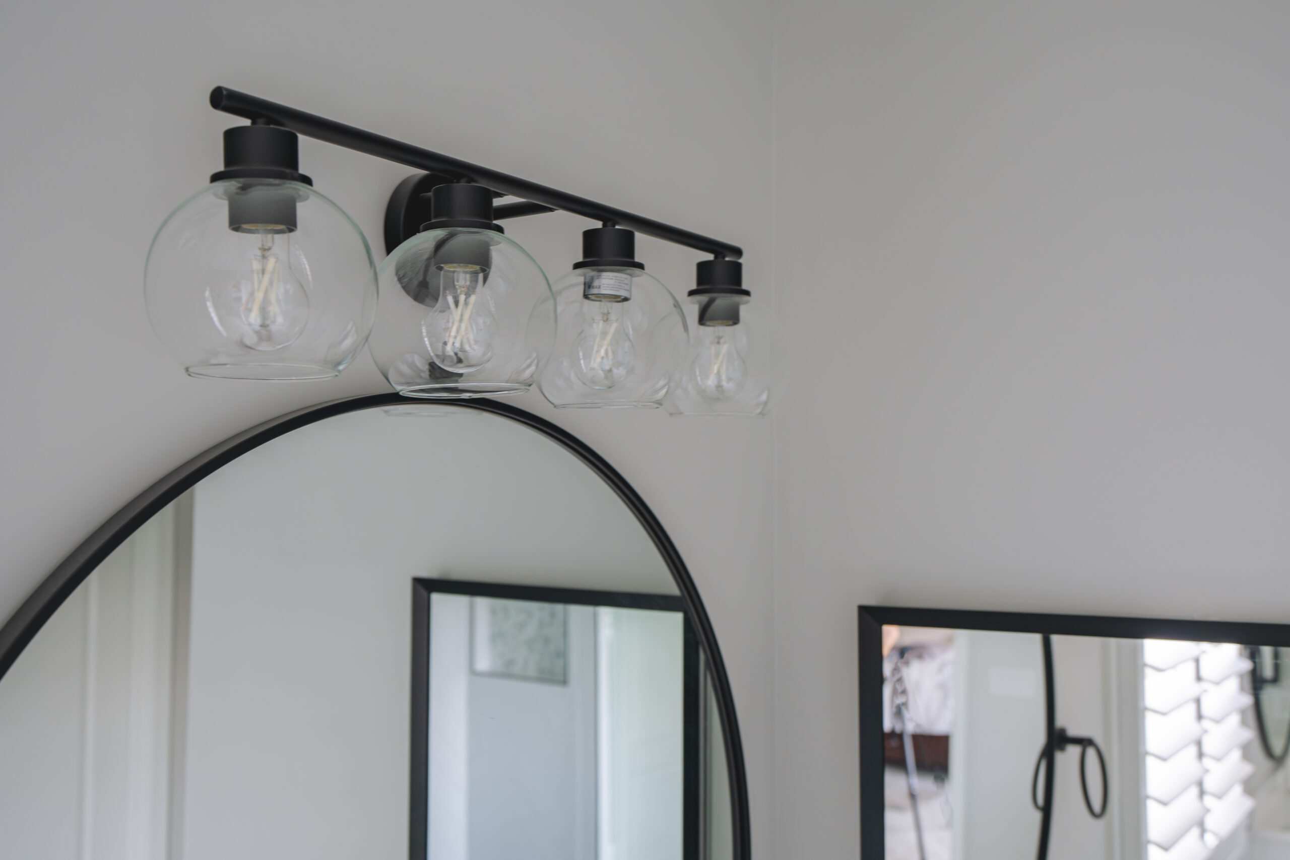 A four-light black vanity fixture with clear glass globes mounted above a round mirror.