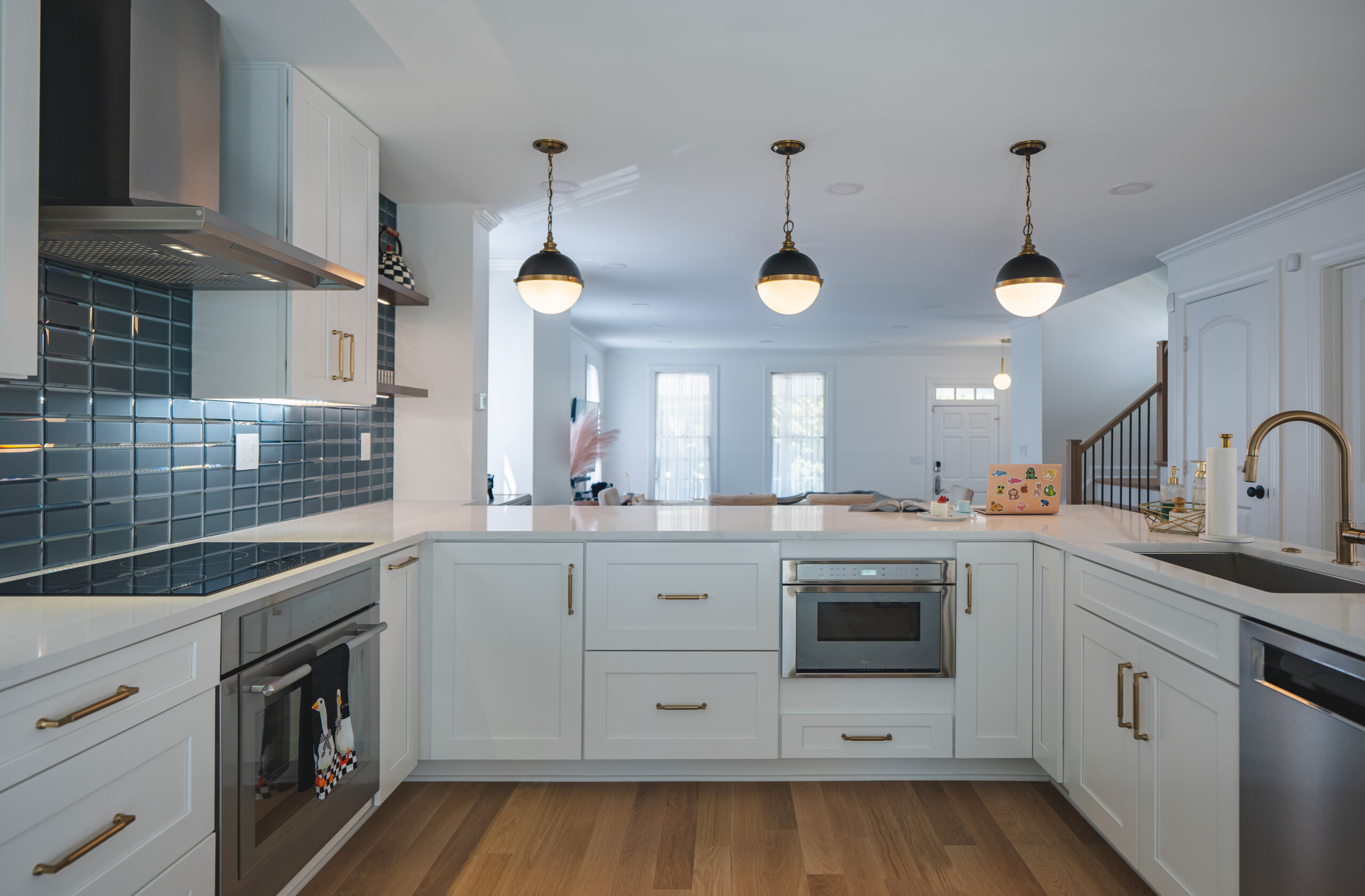 Straight-on view of white shaker-style kitchen cabinets featuring a built-in microwave, stainless steel dishwasher, and teal glass backsplash.