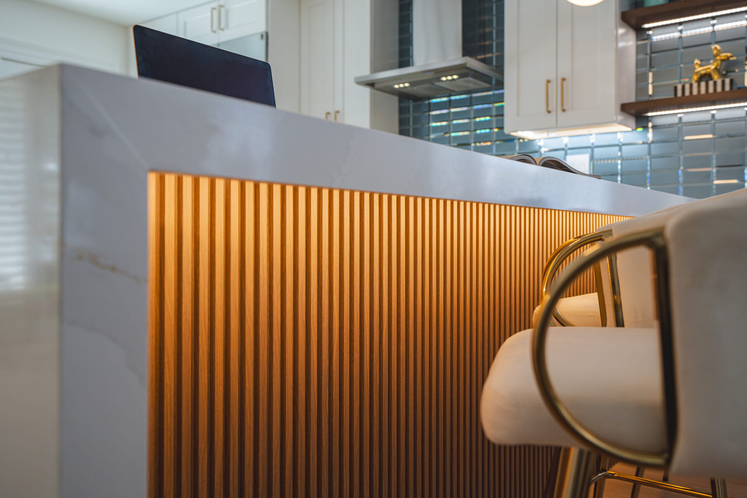 Horizontal close-up of warm LED strip lighting glowing under a white quartz countertop and wood paneling.