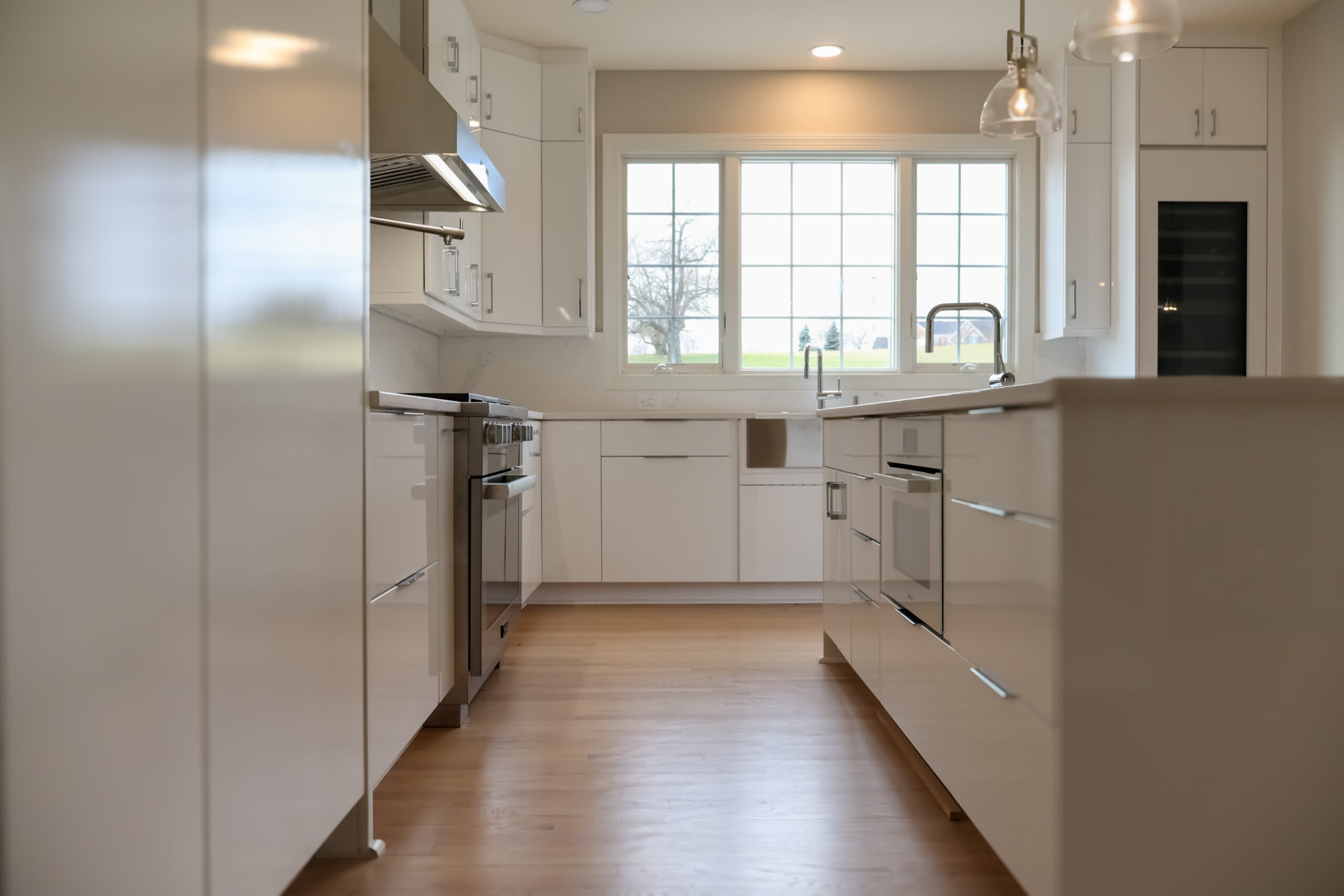 Wide perspective of a kitchen walkway featuring high gloss white custom panels.