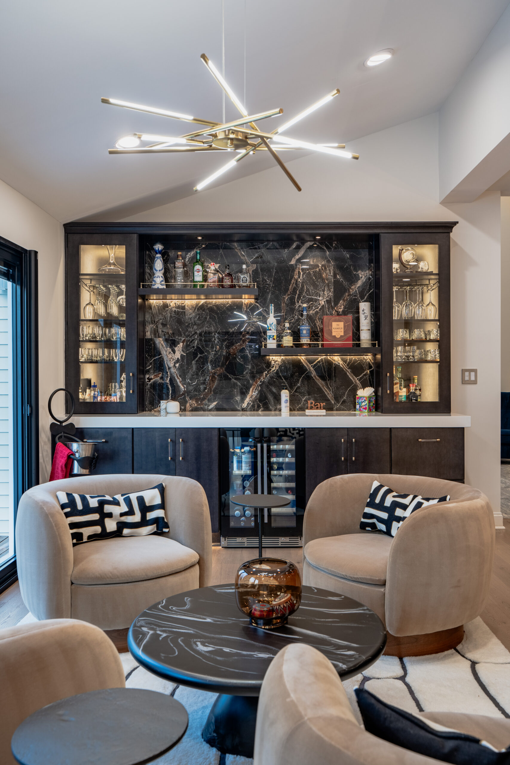 A gold starburst-style chandelier lighting fixture in a renovated living room with a bar area in the background.