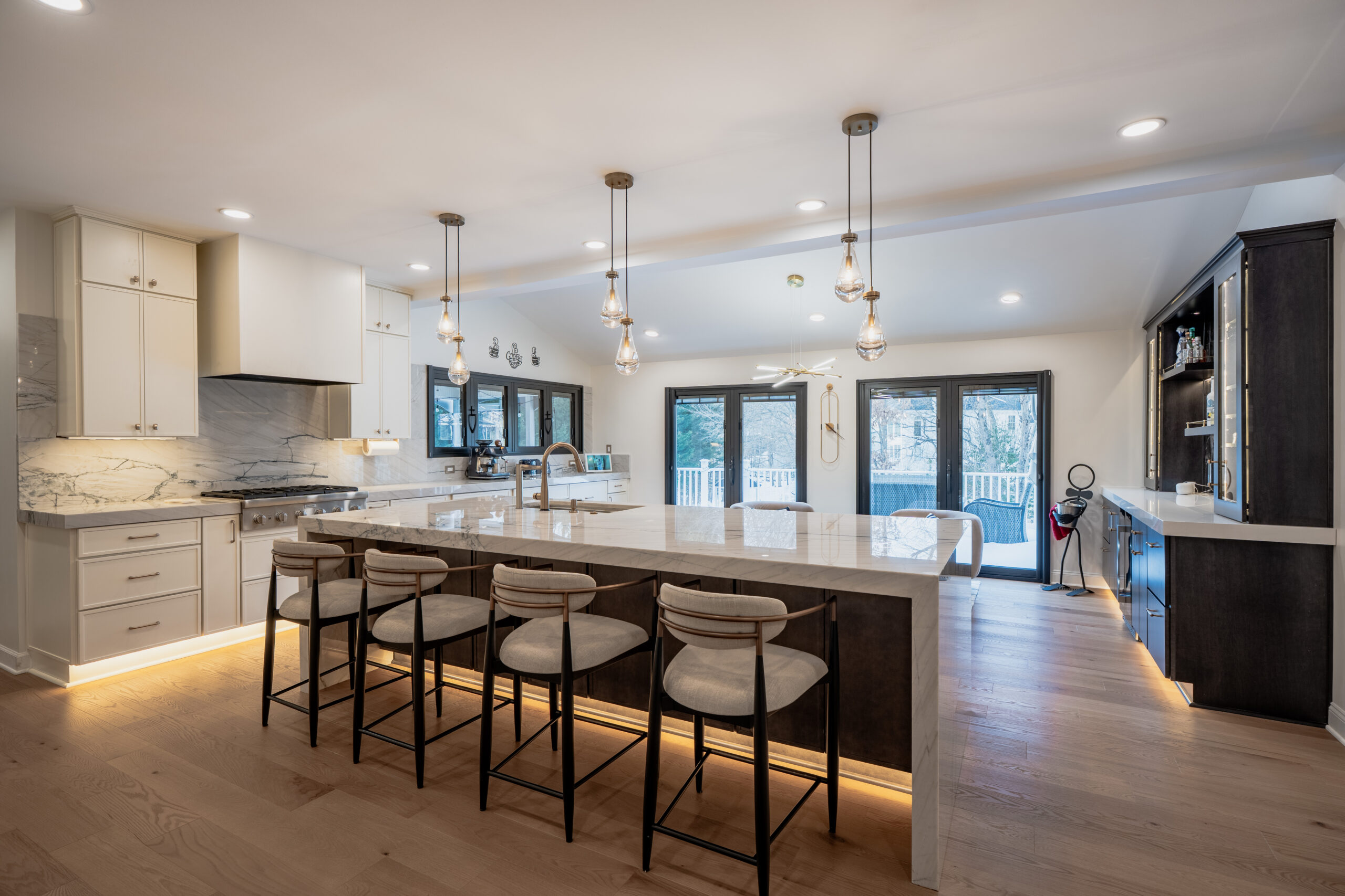 A wide perspective of a remodeled kitchen and living area showing the island seating and a modern home bar in the background.
