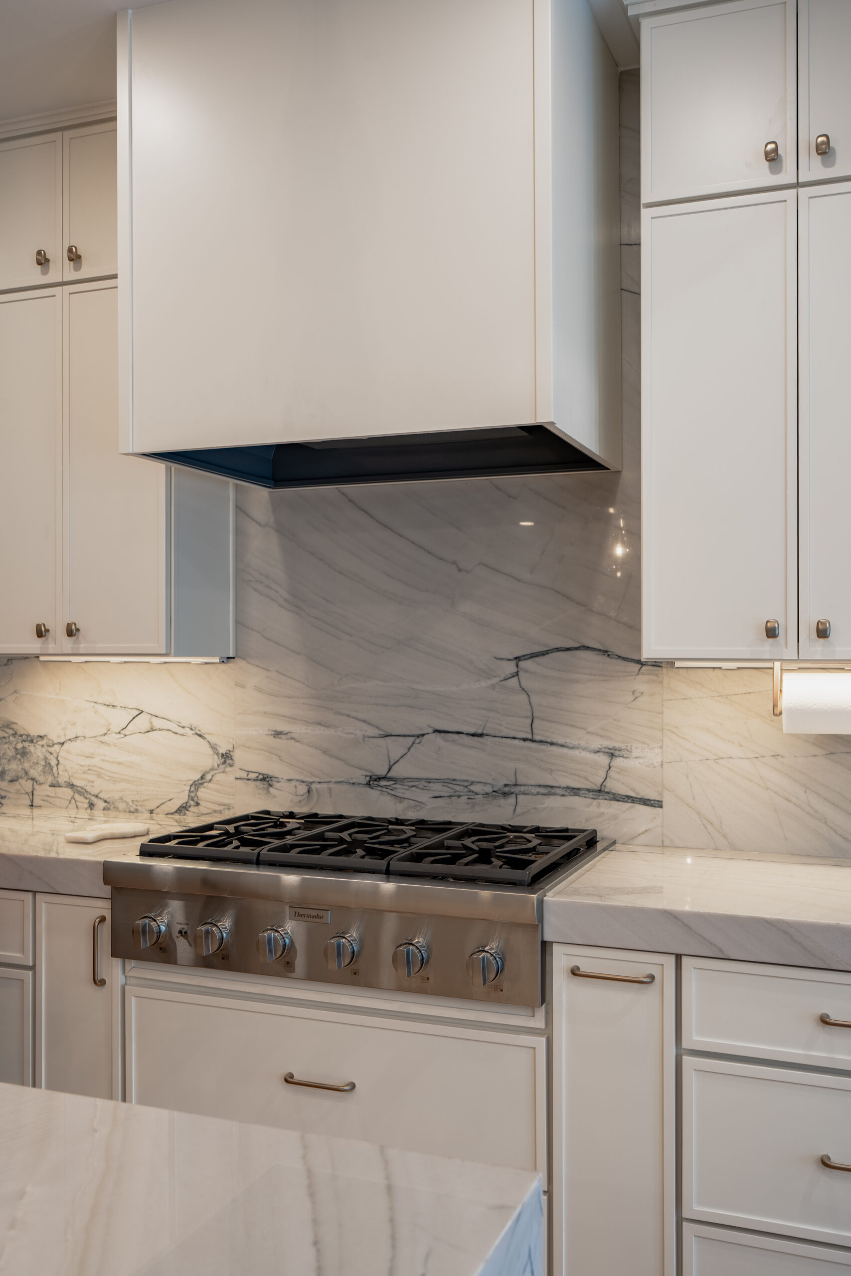 A professional-grade stainless steel gas cooktop set against a solid marble slab backsplash and matching countertops.