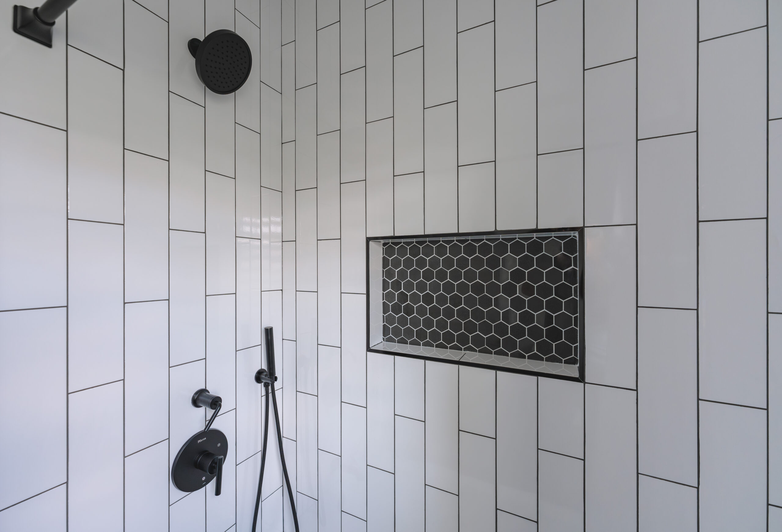 White vertical subway shower tile featuring a recessed niche with black hexagon mosaic backing.
