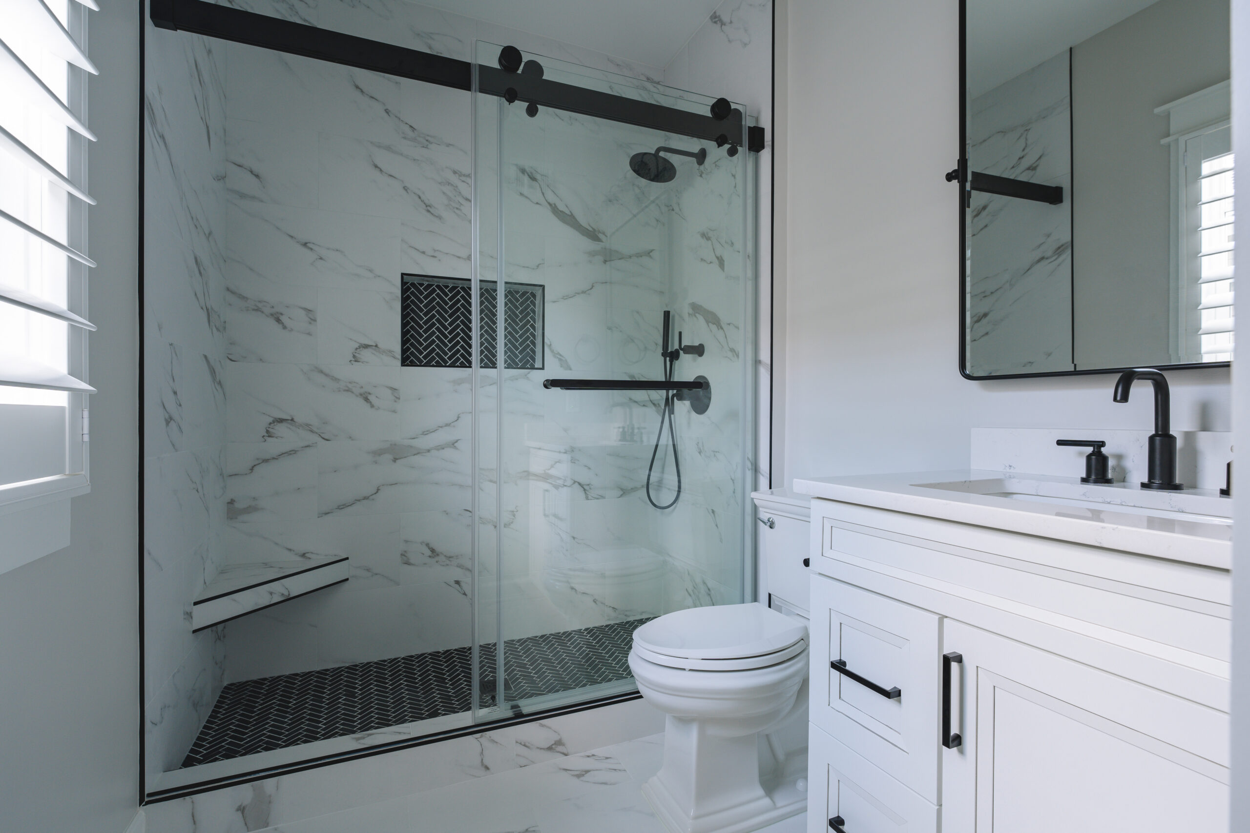 A full bathroom shot showing the sliding glass shower door with black hardware, white vanity, and toilet.