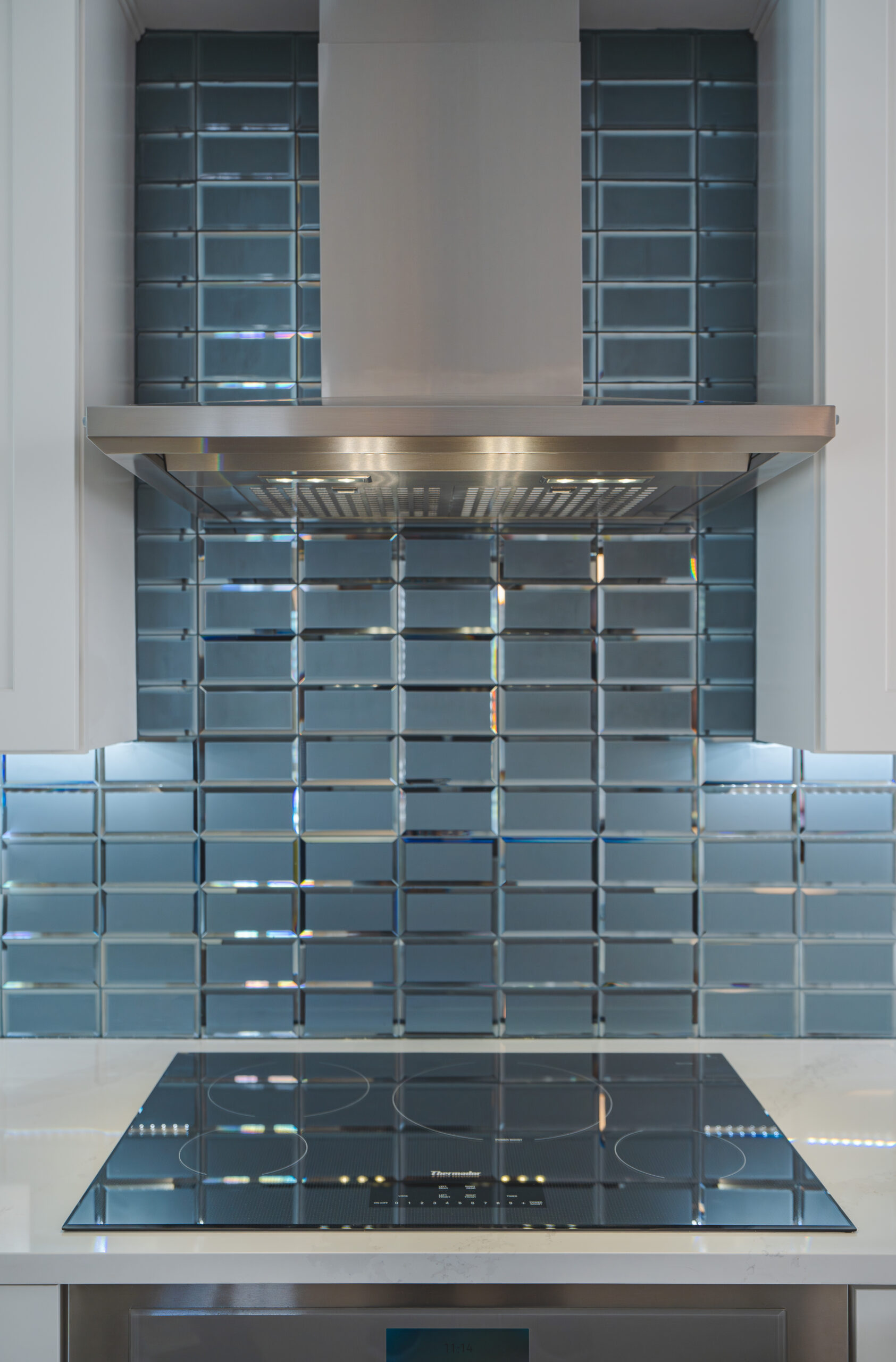 A professional stainless steel range hood mounted against a teal glass subway tile wall over an induction cooktop.