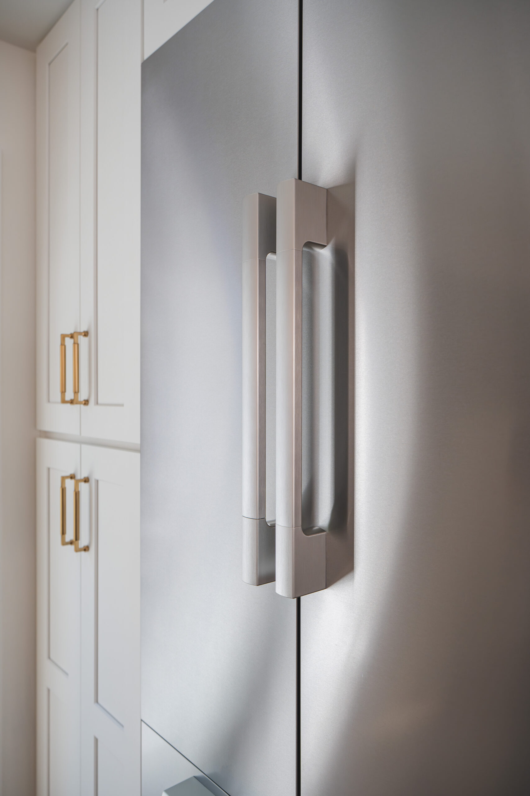 A close-up of a stainless steel refrigerator handle with gold-accented white cabinets in the background.