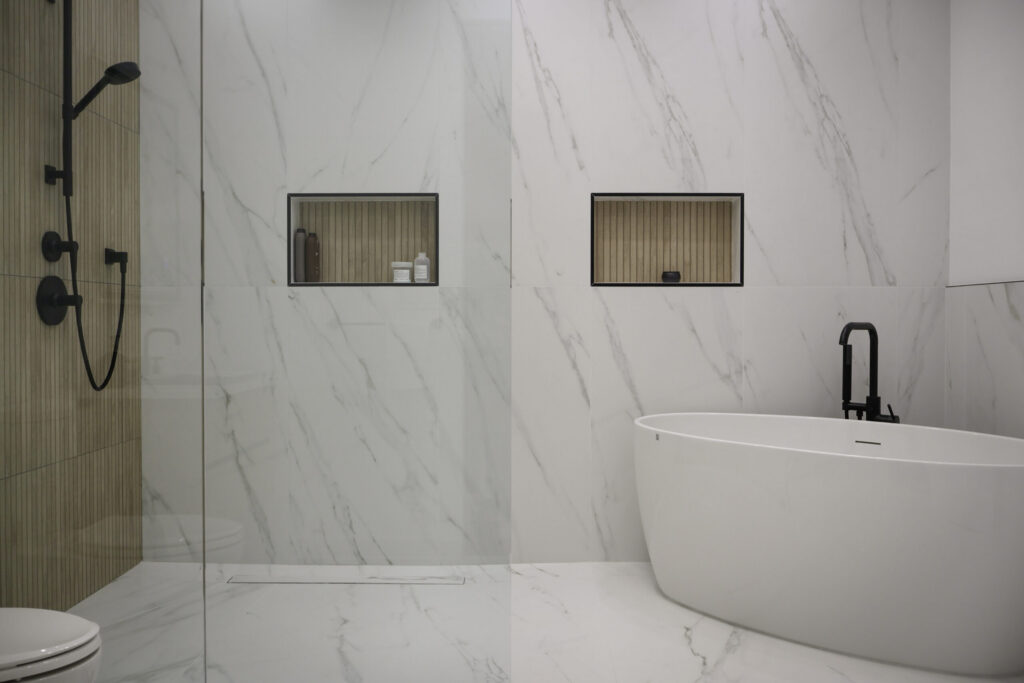 A spacious, elegant bathroom featuring a warm wood laminate floor, white cabinetry with a built-in vanity, and a large soaking tub accented by a marble stone backsplash and glass-enclosed shower.