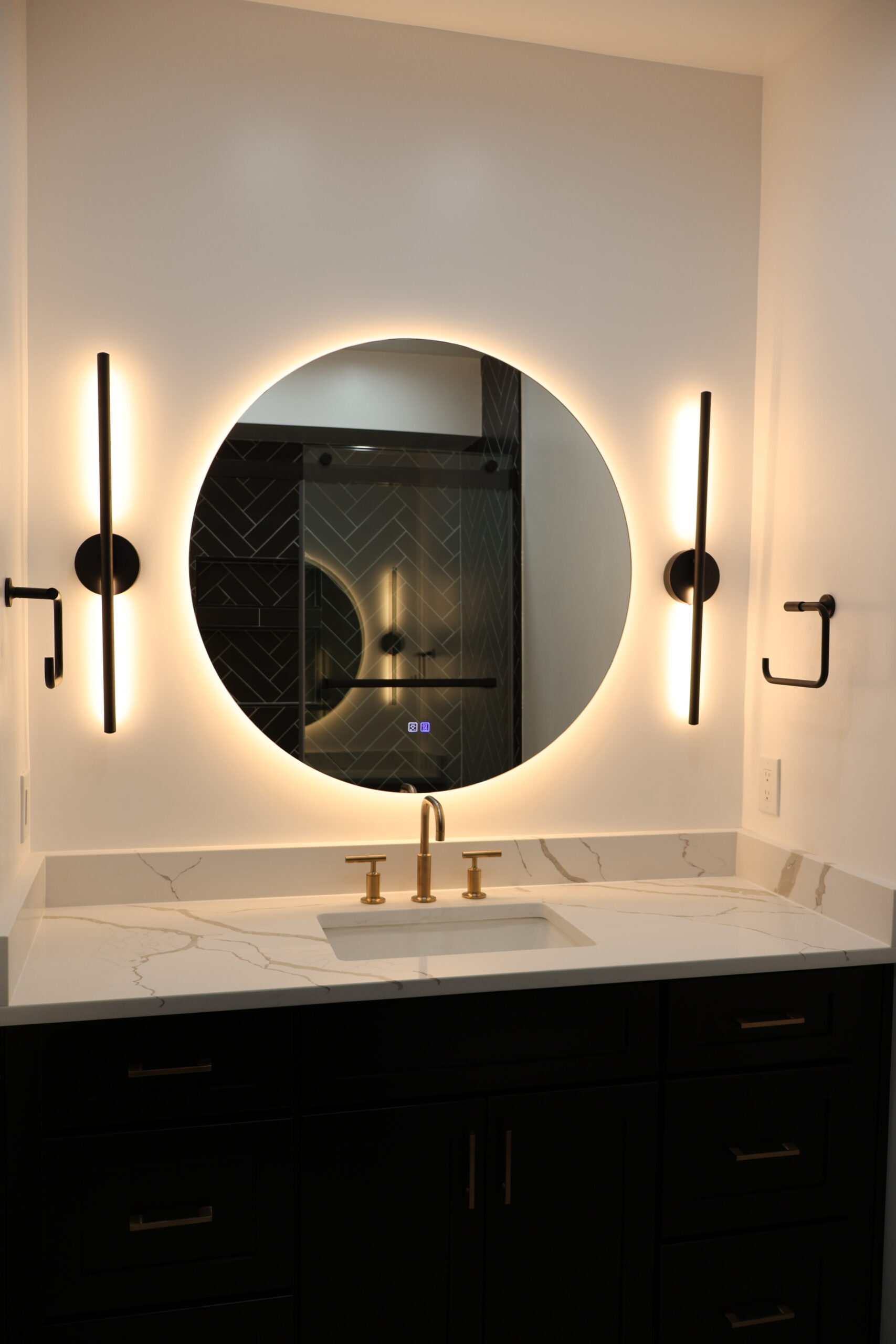 Symmetrical bathroom vanity view with twin vertical stick sconces and gold hardware.